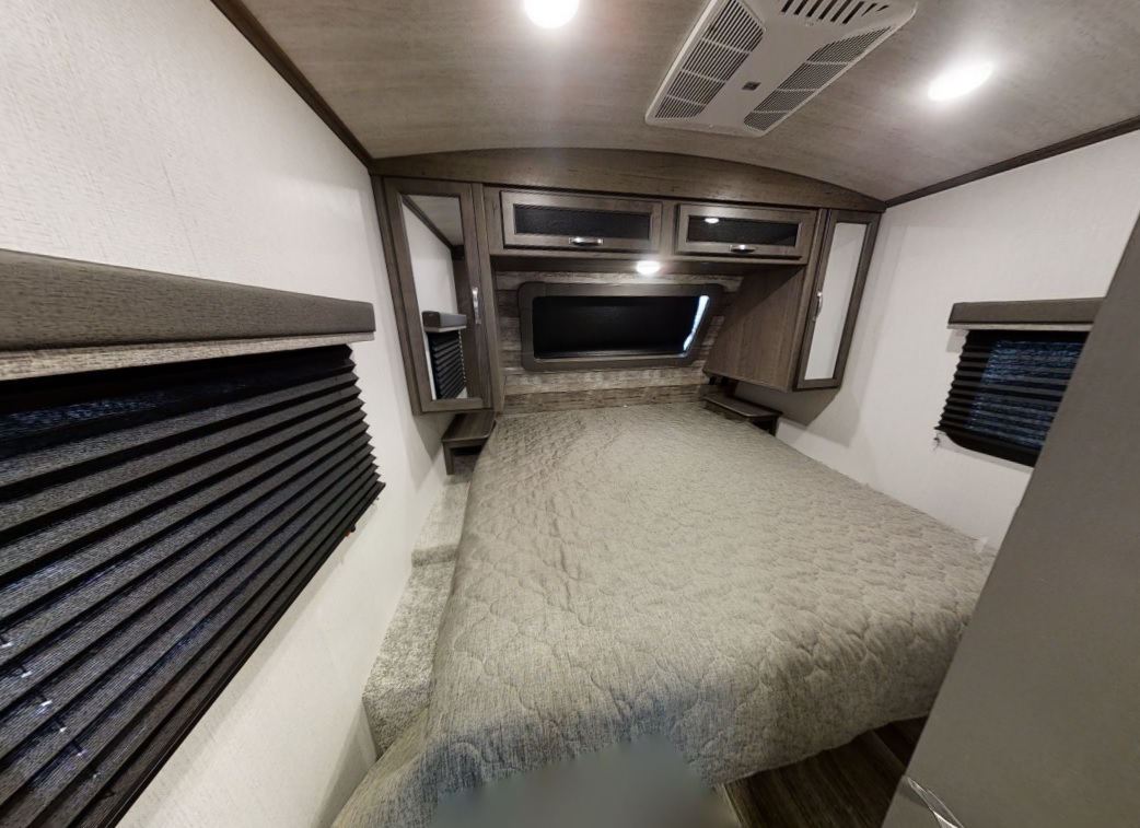 This RV rental's bedroom features a comfortable bed with a light comforter, overhead storage, and dark window blinds.. Keystone Cougar Half-Ton 2021