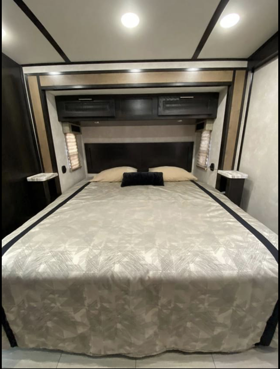 Modern RV rental bedroom with a large bed, dark headboard, overhead cabinets, and built-in nightstands for comfort.. Forest River Fr3 2019