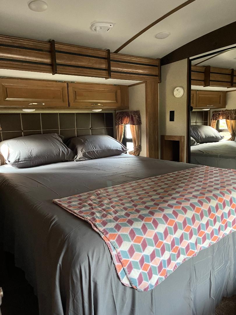 Cozy RV rental bedroom featuring a large bed with gray bedding, a vibrant geometric blanket, and ample overhead storage.. Keystone RV Laredo 2022