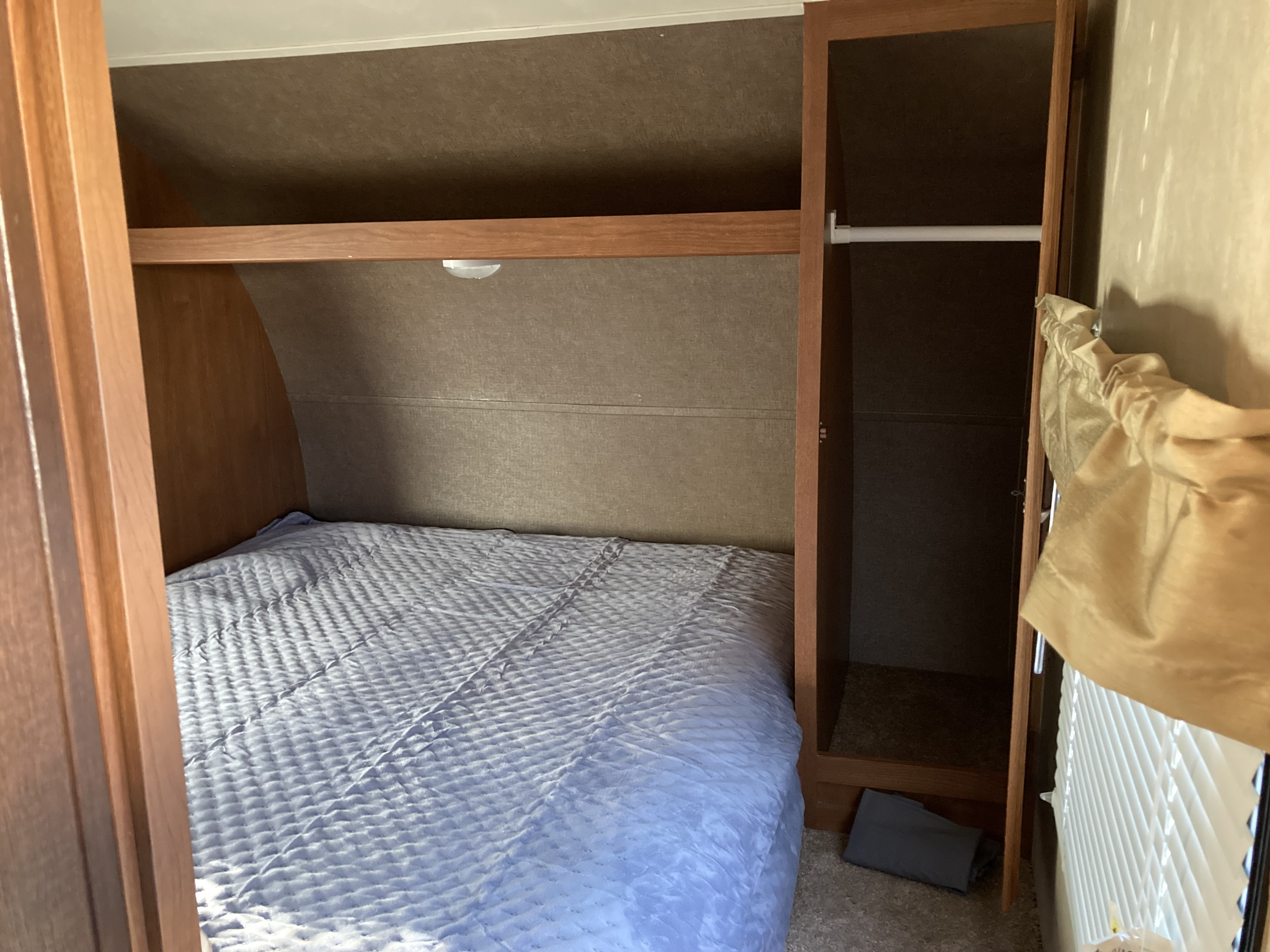 RV rental: Compact bedroom featuring a light blue quilted bed, wooden storage shelf, and a narrow closet.. Forest River Wildwood X-Lite 2016