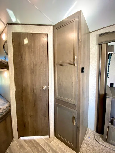 Inside an RV rental: a wood-grain door, corner storage cabinet, and bedroom glimpse. Compact living space.. Jayco Jay Flight 2021