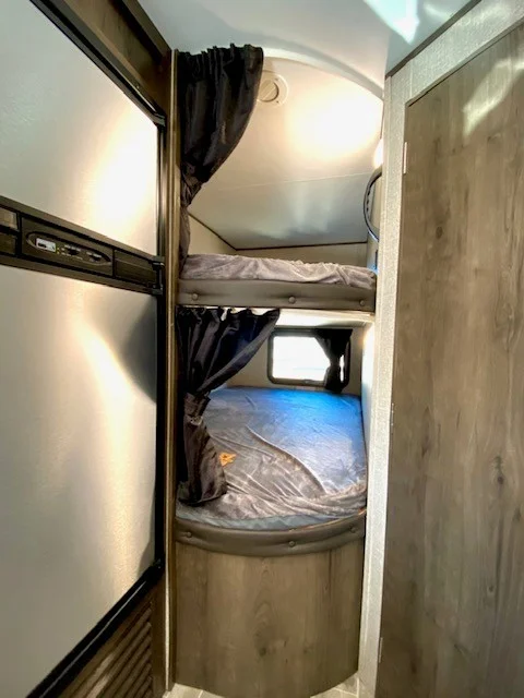 Explore this RV rental's cozy bunk beds: a top/bottom setup with privacy curtains, beside a fridge.. Jayco Jay Flight 2021