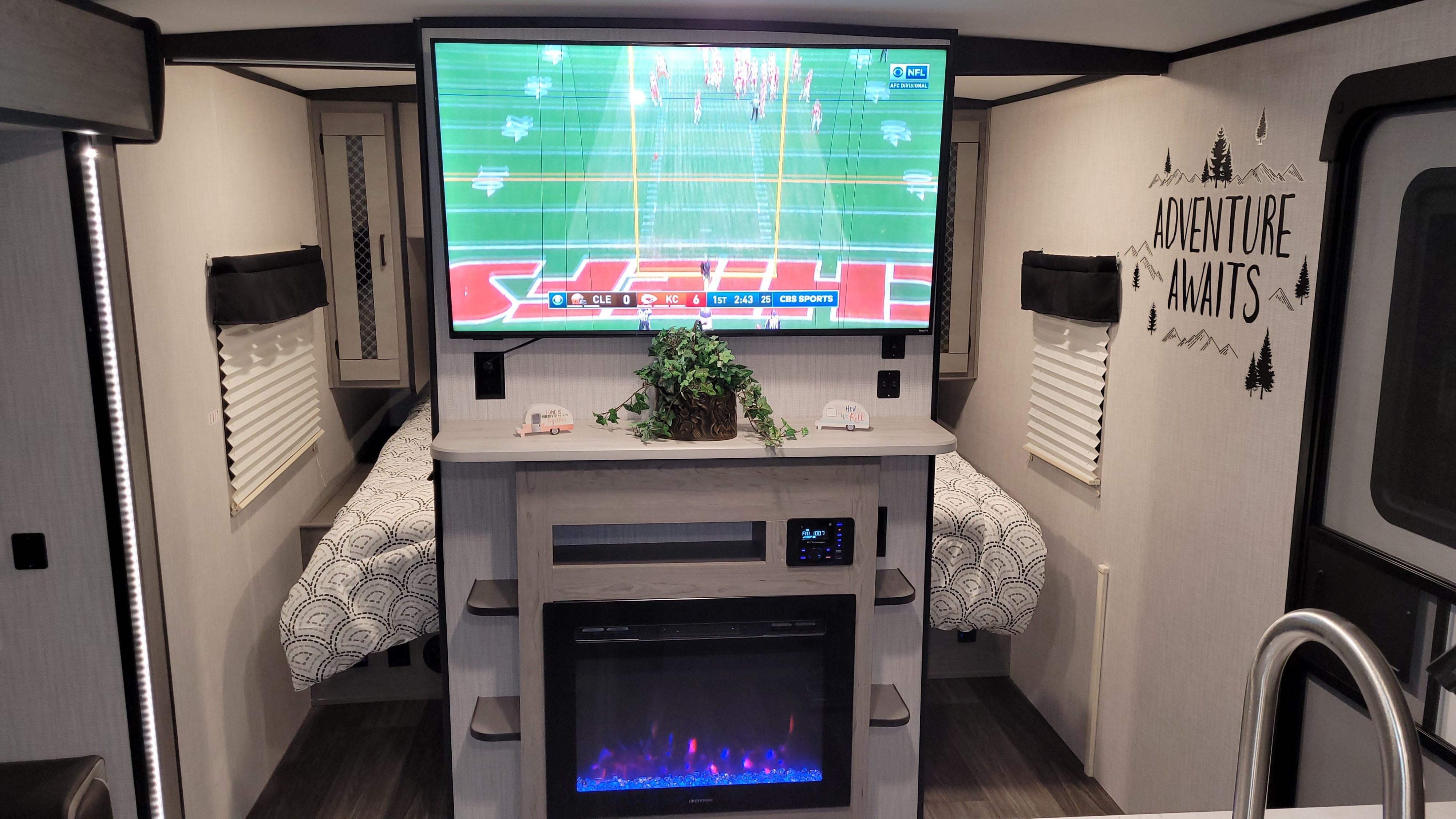 Cozy RV rental interior featuring a TV with an NFL game, electric fireplace, and two beds. Perfect for adventure!. Other Other 2021
