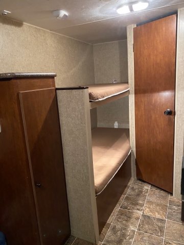 RV rental interior: two bunk beds with brown mattresses, a wooden wardrobe on the left, and a door on the right.. K-Z Manufacturing Spree Escape 2014