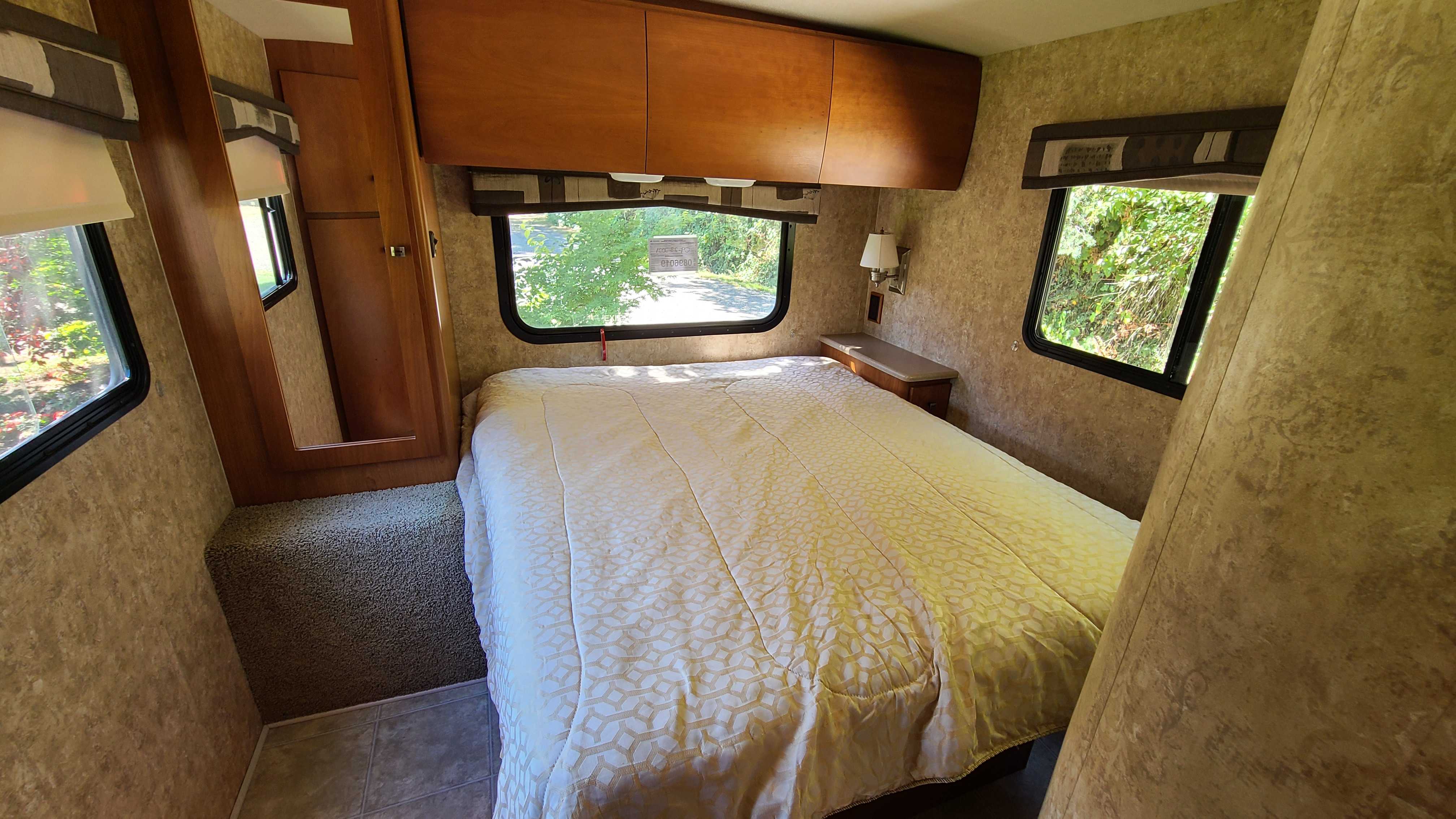 This cozy RV rental bedroom features a comfy bed, windows with nature views, and functional storage.. Itasca Spirit 2007