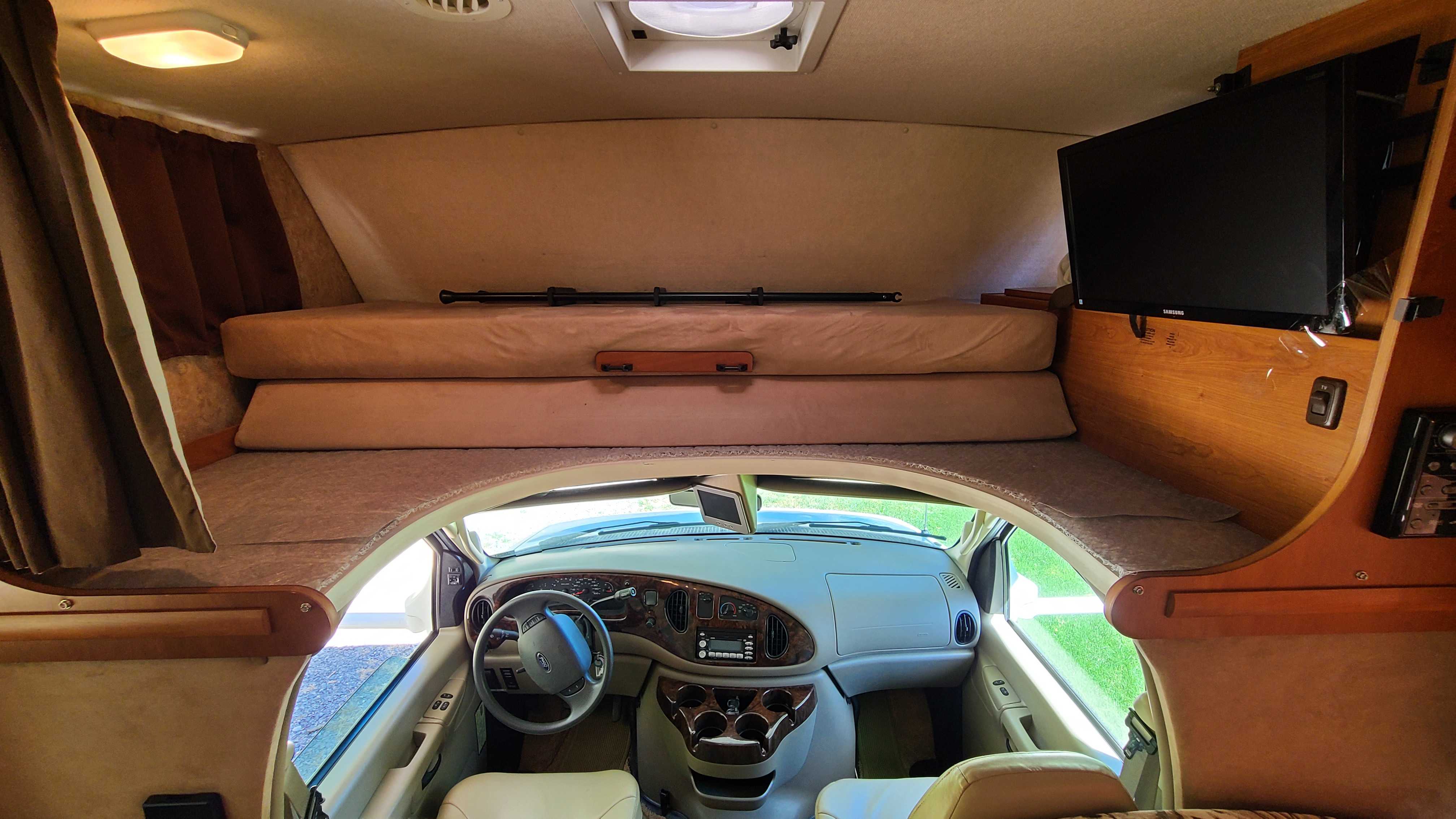 Spacious RV rental interior featuring an over-cab bed, TV, and driver's cockpit. Ideal for your next road trip adventure.. Itasca Spirit 2007