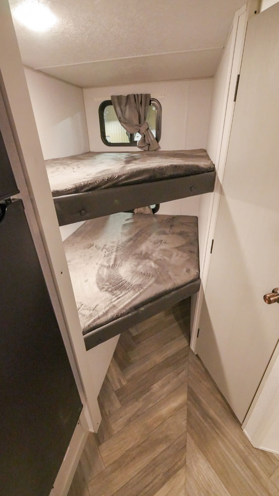 Inside an RV rental: Compact bunk beds with grey mattresses and a window, ideal for extra sleeping space.. Forest River Wildwood FSX Platinum 2021