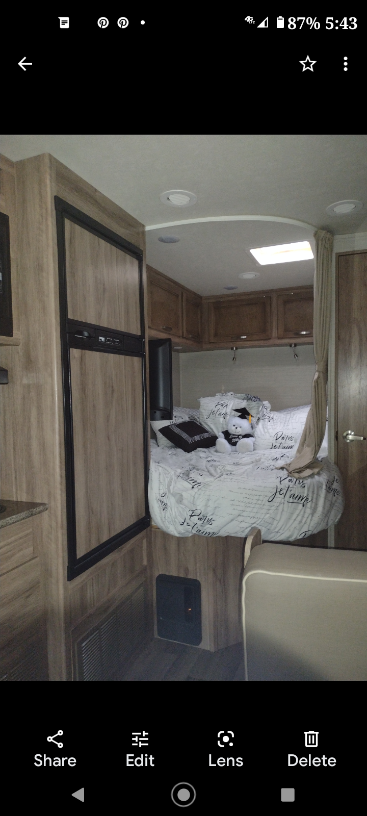 Cozy RV rental interior shows a compact bed with white script bedding, built-in fridge, and wooden cabinets.. Jayco Redhawk SE 2020
