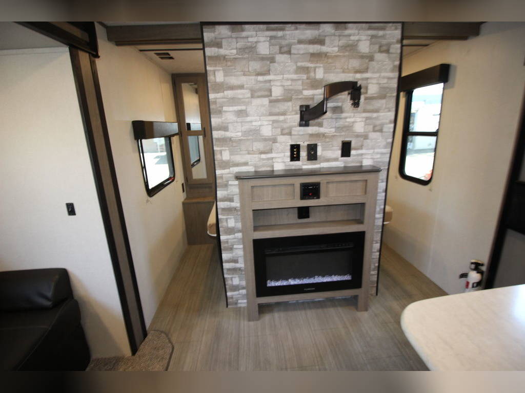 Inside a modern rv rental: living area with faux stone accent wall, TV mount, electric fireplace, and light wood flooring.. Keystone Hideout 2020