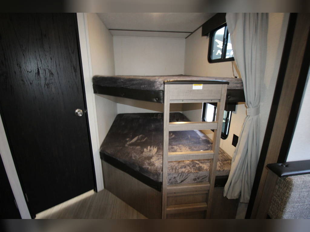 This RV rental interior features a cozy bunk bed setup with ladder, private door, and windows, offering comfortable sleeping for travelers.. Keystone Hideout 2020