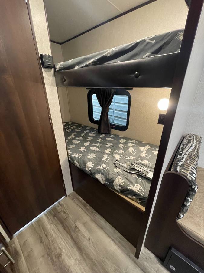 Inside an RV rental: a cozy sleeping area featuring bunk beds with patterned bedding, a window, and a reading light.. Jayco Jay Flight 2019