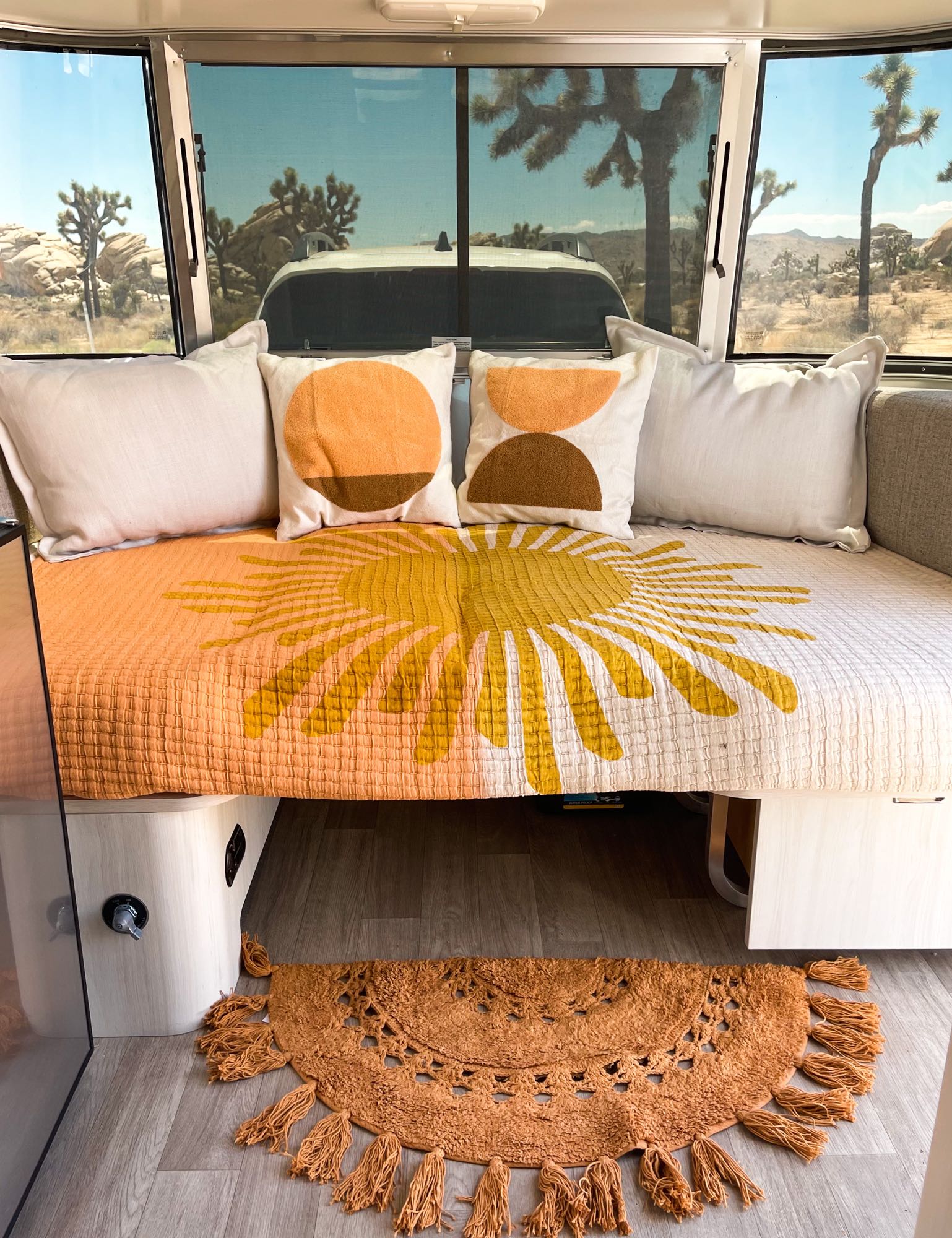 Cozy rv rental interior with sun-patterned bedding, accent pillows, and a tassel rug. Outside, Joshua Tree desert views.. Airstream Bambi 2021
