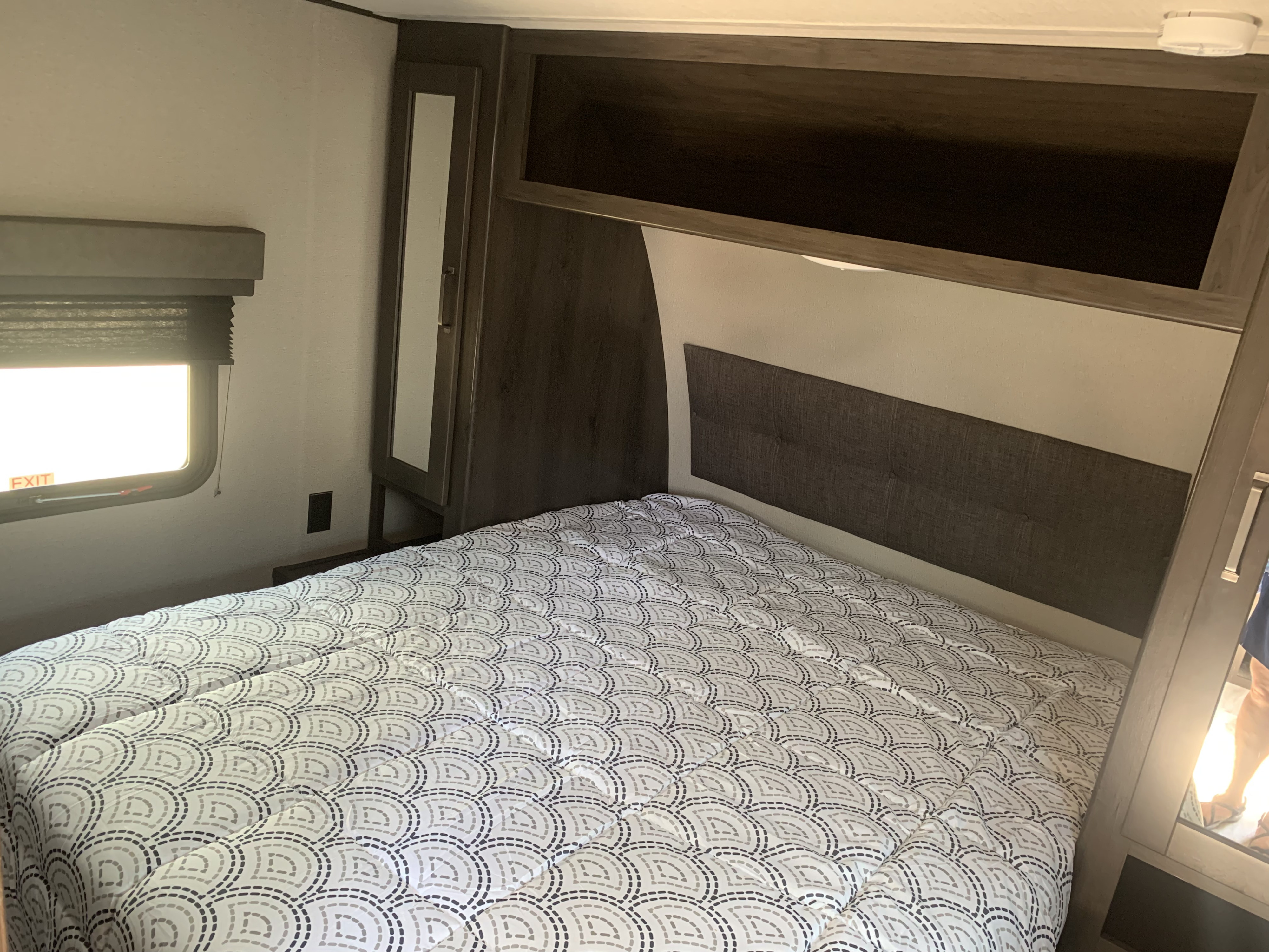 RV rental bedroom: a bed with patterned comforter, built-in storage, and window displaying an 'EXIT' sign.. Grand Design Transcend 2022