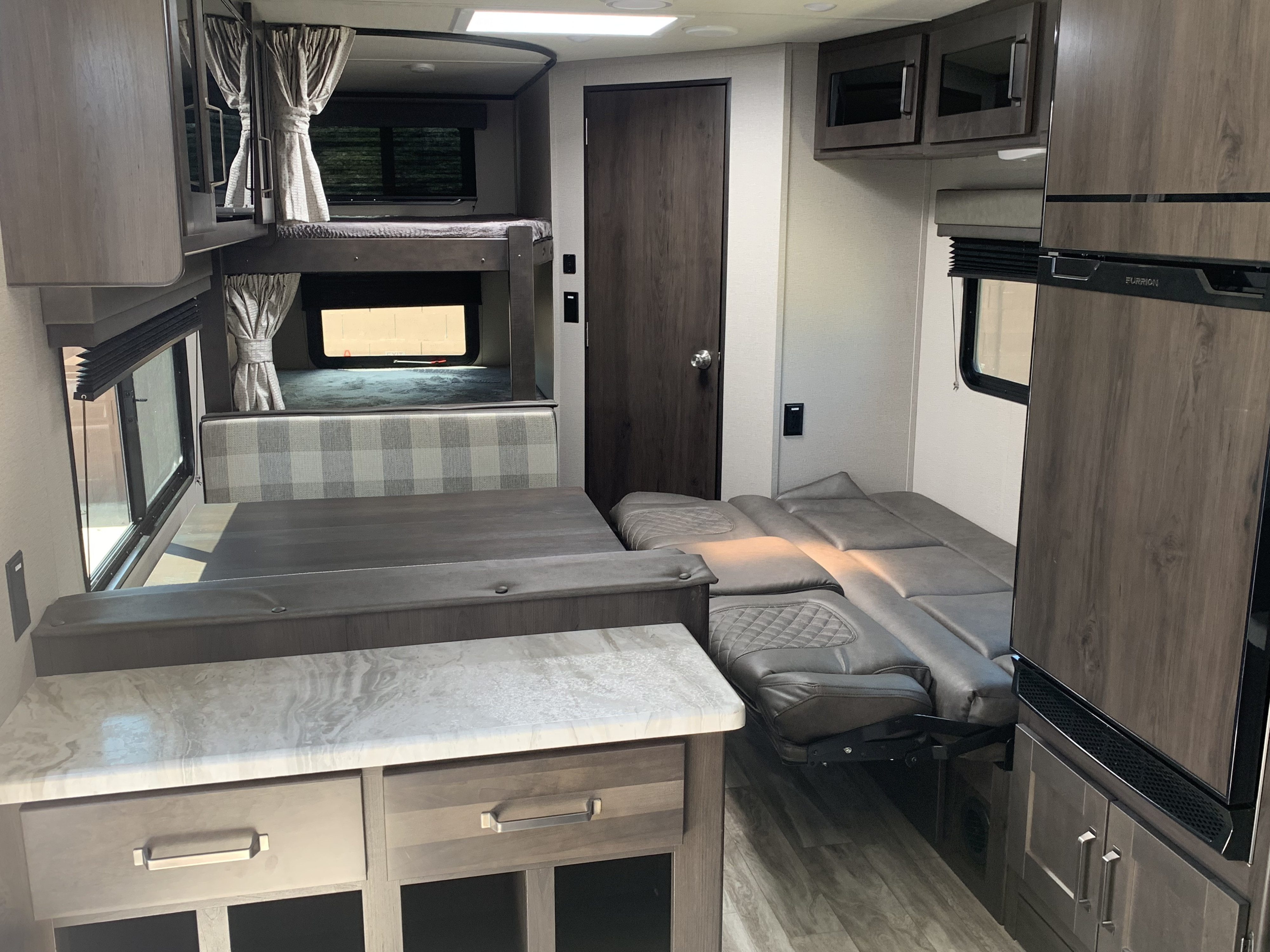 RV rental interior featuring bunk beds, a convertible dinette, a sleeper sofa, and a kitchen area with refrigerator.. Grand Design Transcend 2022