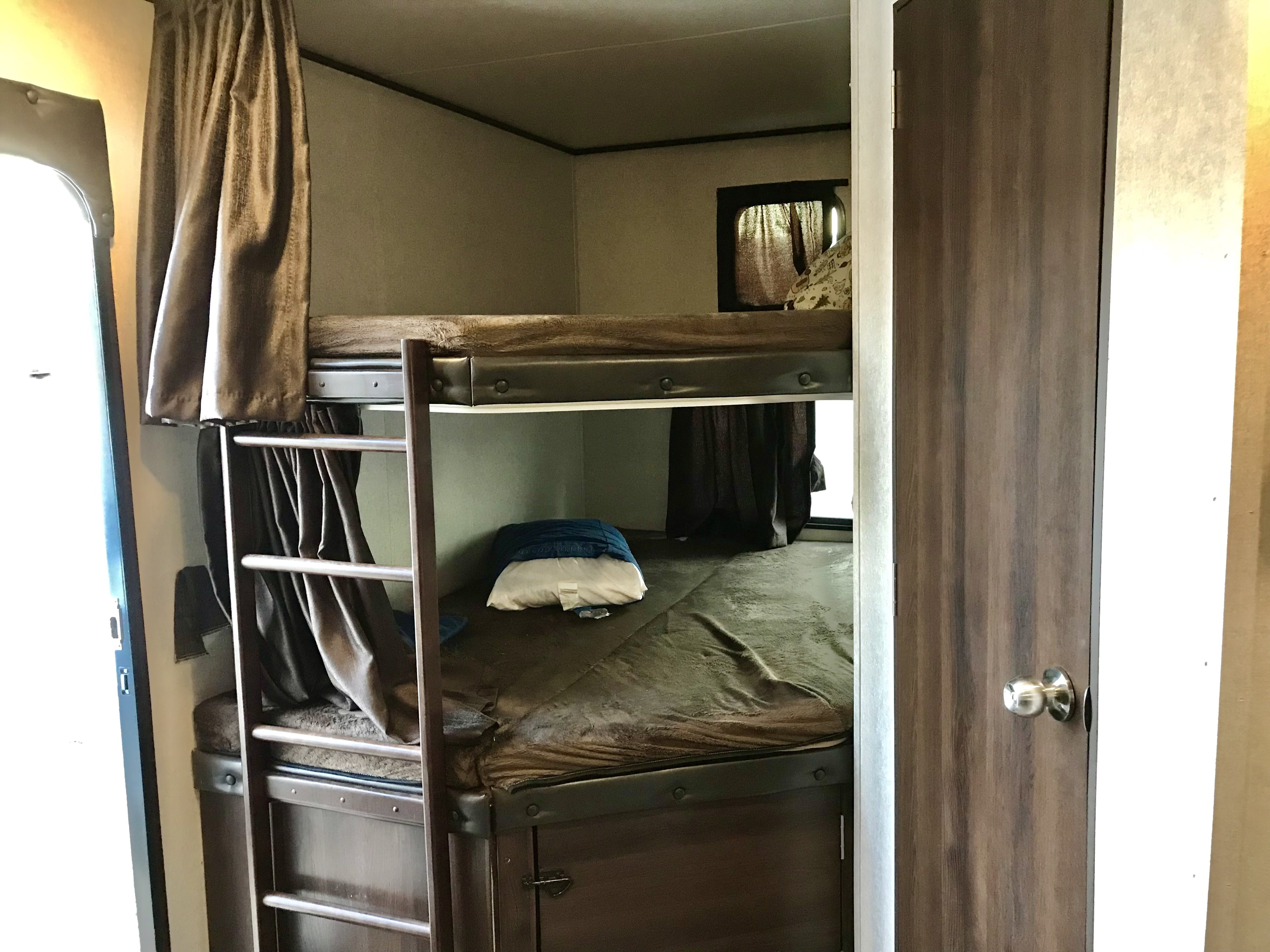 Inside an RV rental: two bunk beds with dark bedding & curtains provide compact sleeping space. A ladder is visible on the left.. Jayco Jay Flight 2019