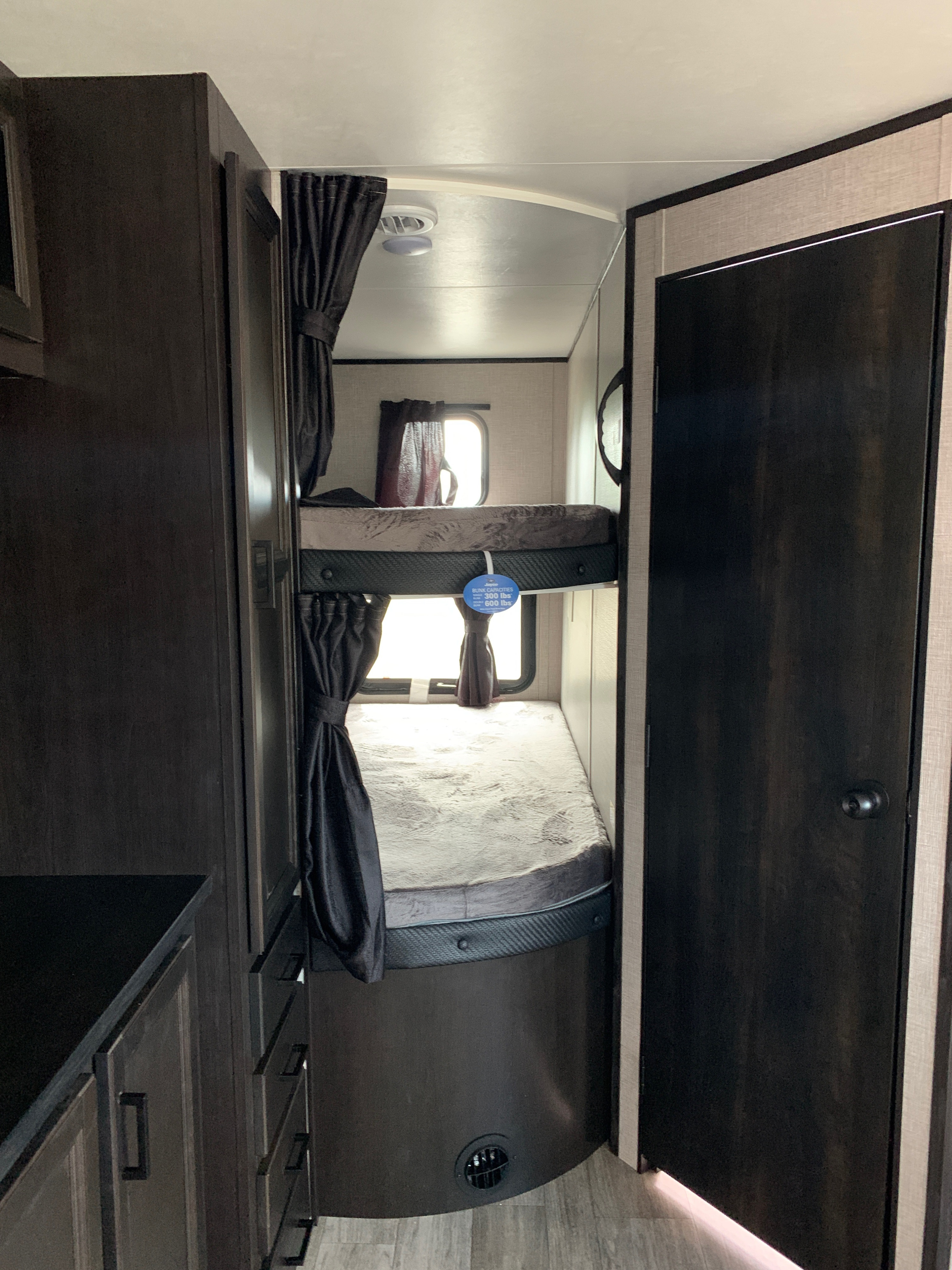 Dark wood RV rental interior featuring two bunk beds with privacy curtains & windows. Ideal for family trips.. Jayco Jay Flight 2021