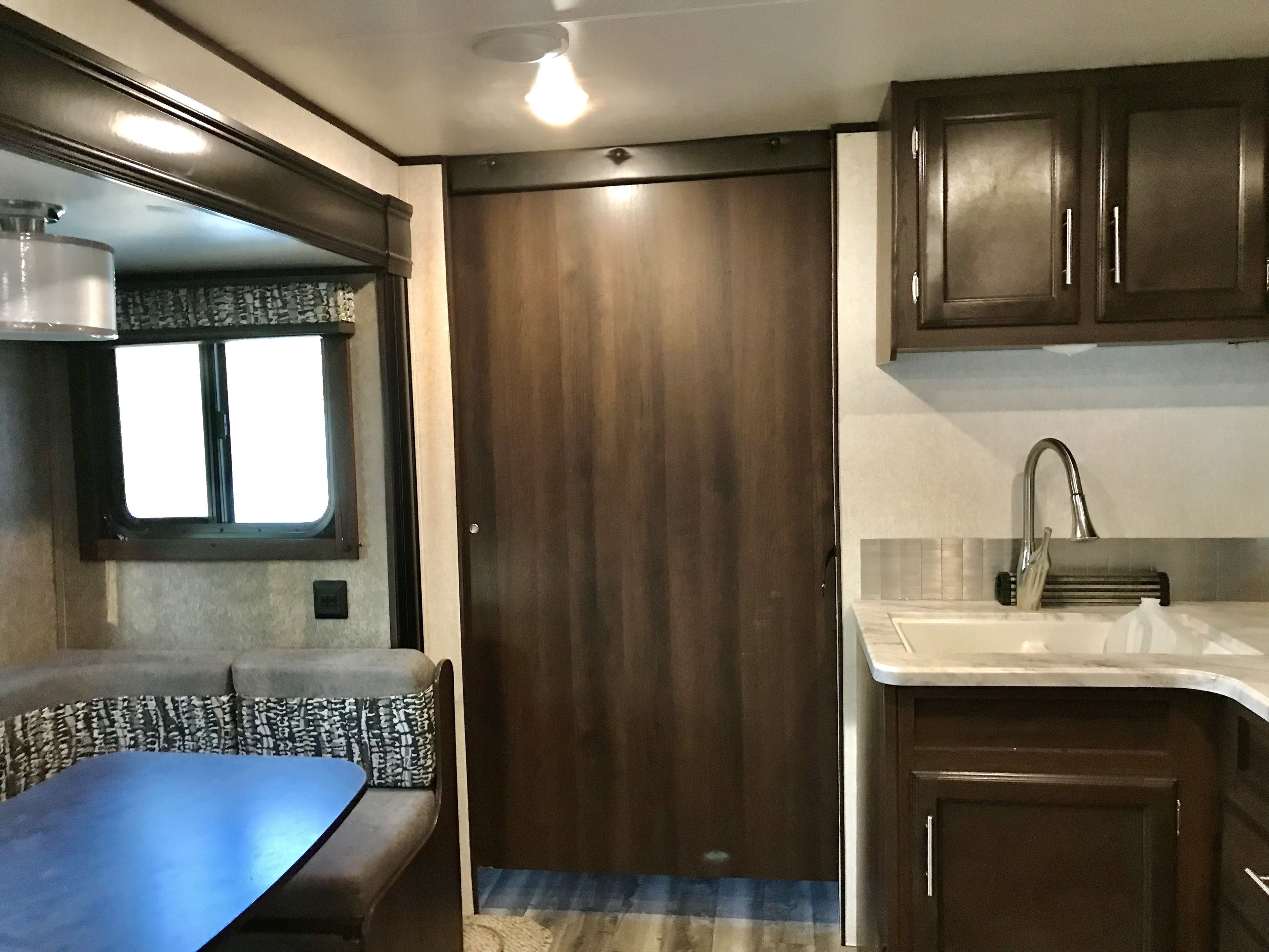 Inside this RV rental, a kitchen area with sink and dark cabinets, plus a dining booth and private door.. Jayco Jay Flight 2019