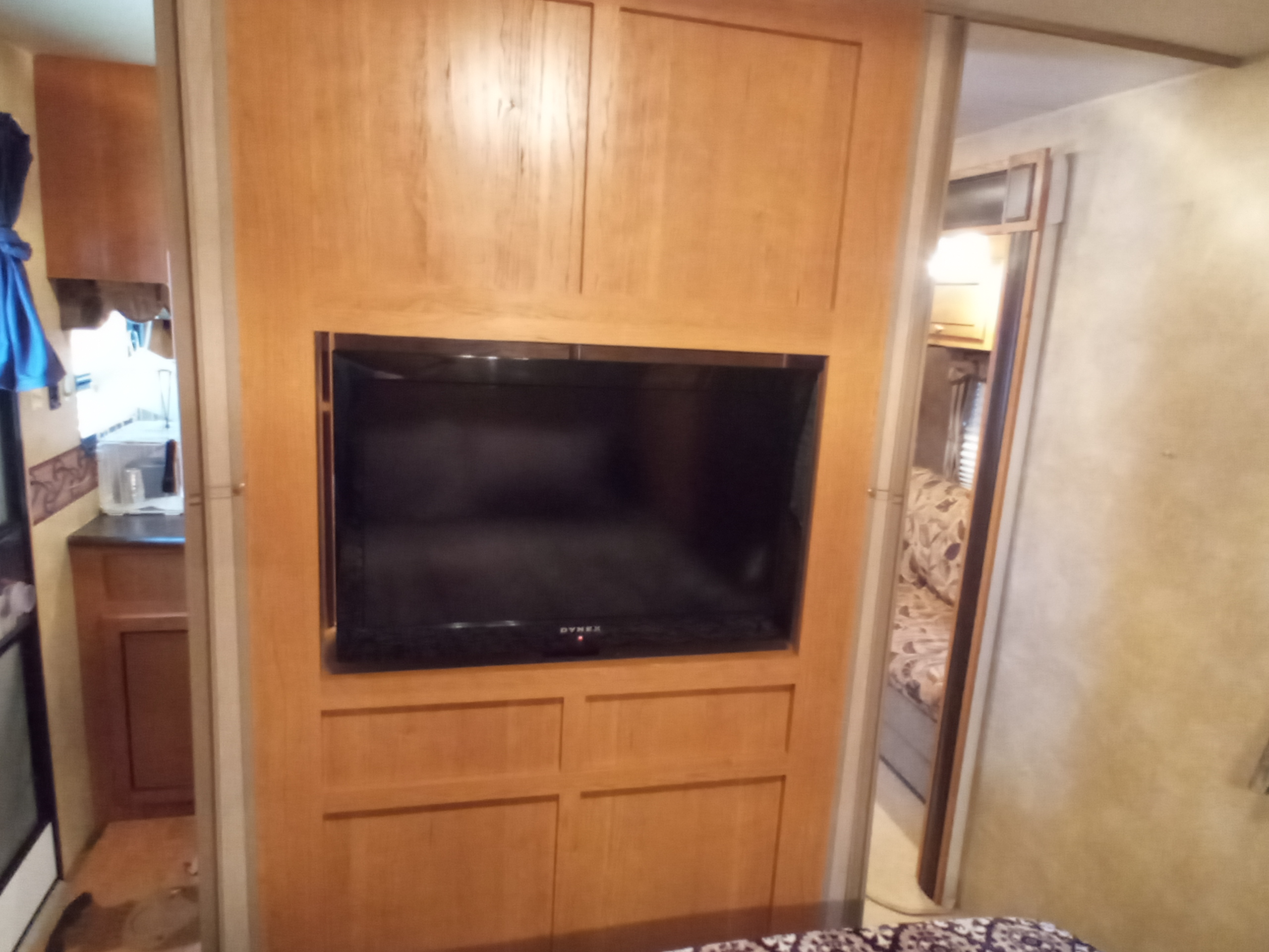 RV rental interior featuring a wooden entertainment unit with a Dynex TV, glimpses of kitchen and bedroom.. Holiday rambler Traveler 2013