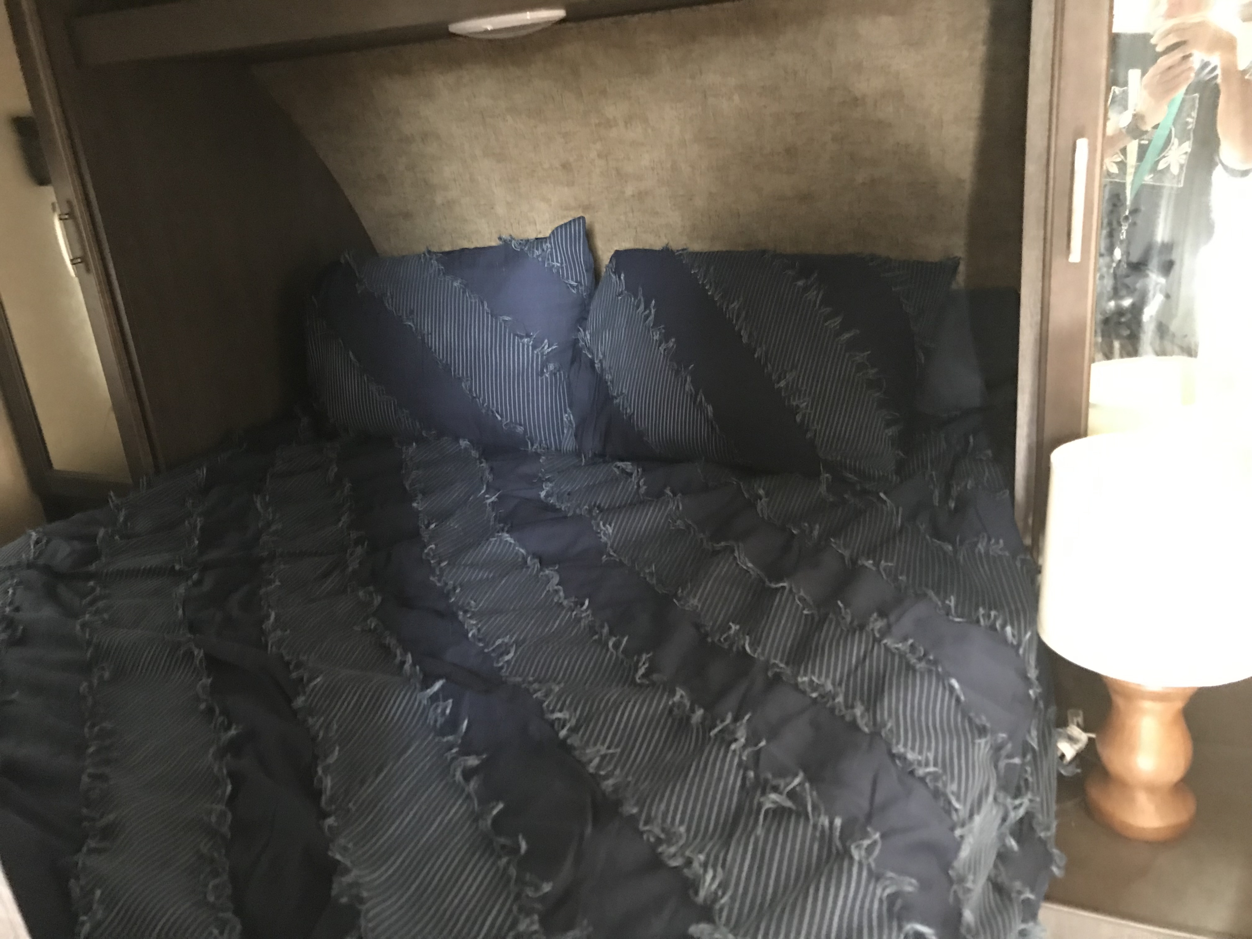 RV rental bedroom with a navy blue striped bed, matching pillows, overhead storage, and a bedside lamp.. Forest River Forester 2017
