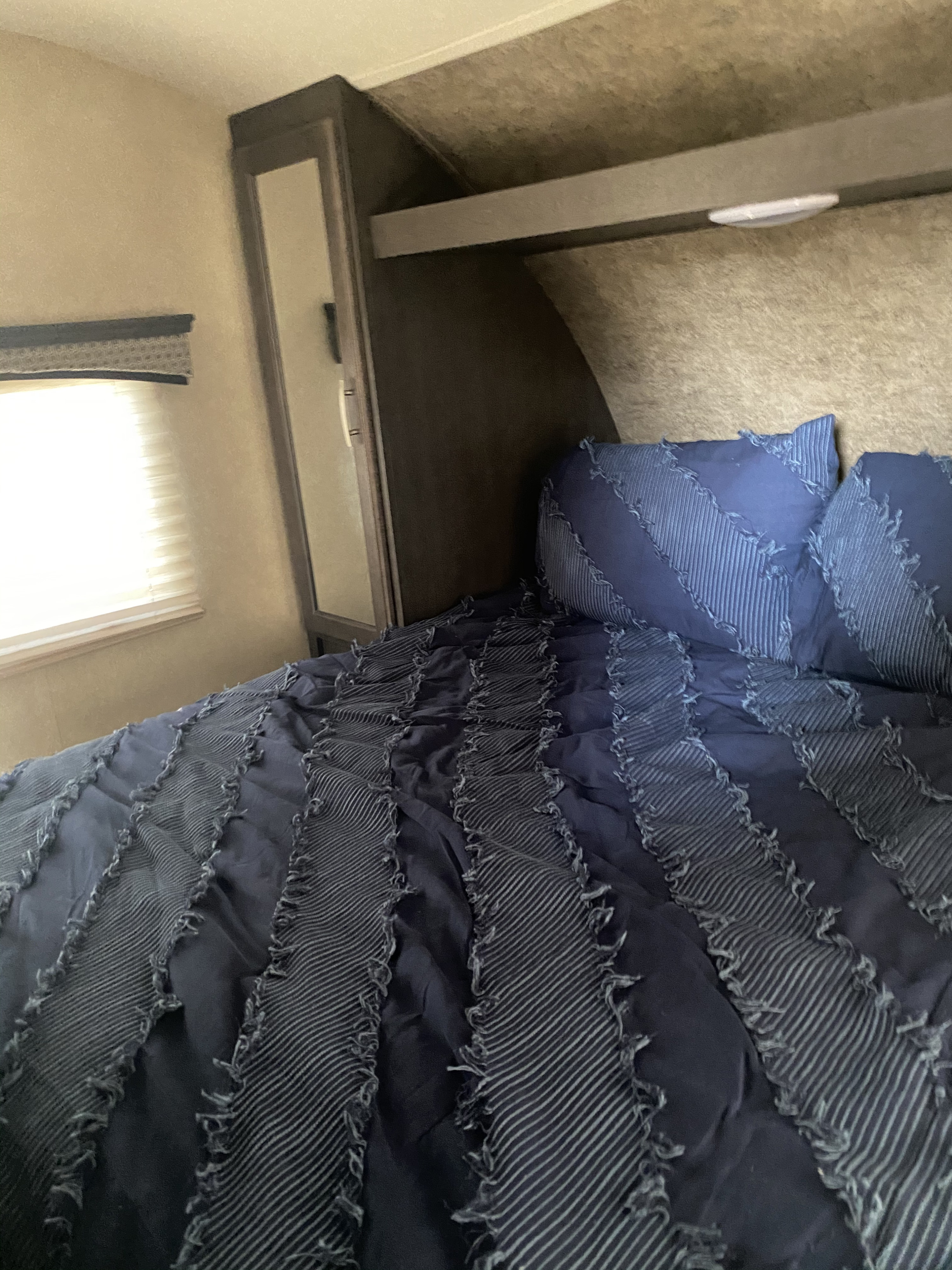 Cozy RV rental bedroom with blue bedding, mirror, and window. Perfect for your next adventure!. Forest River Forester 2017