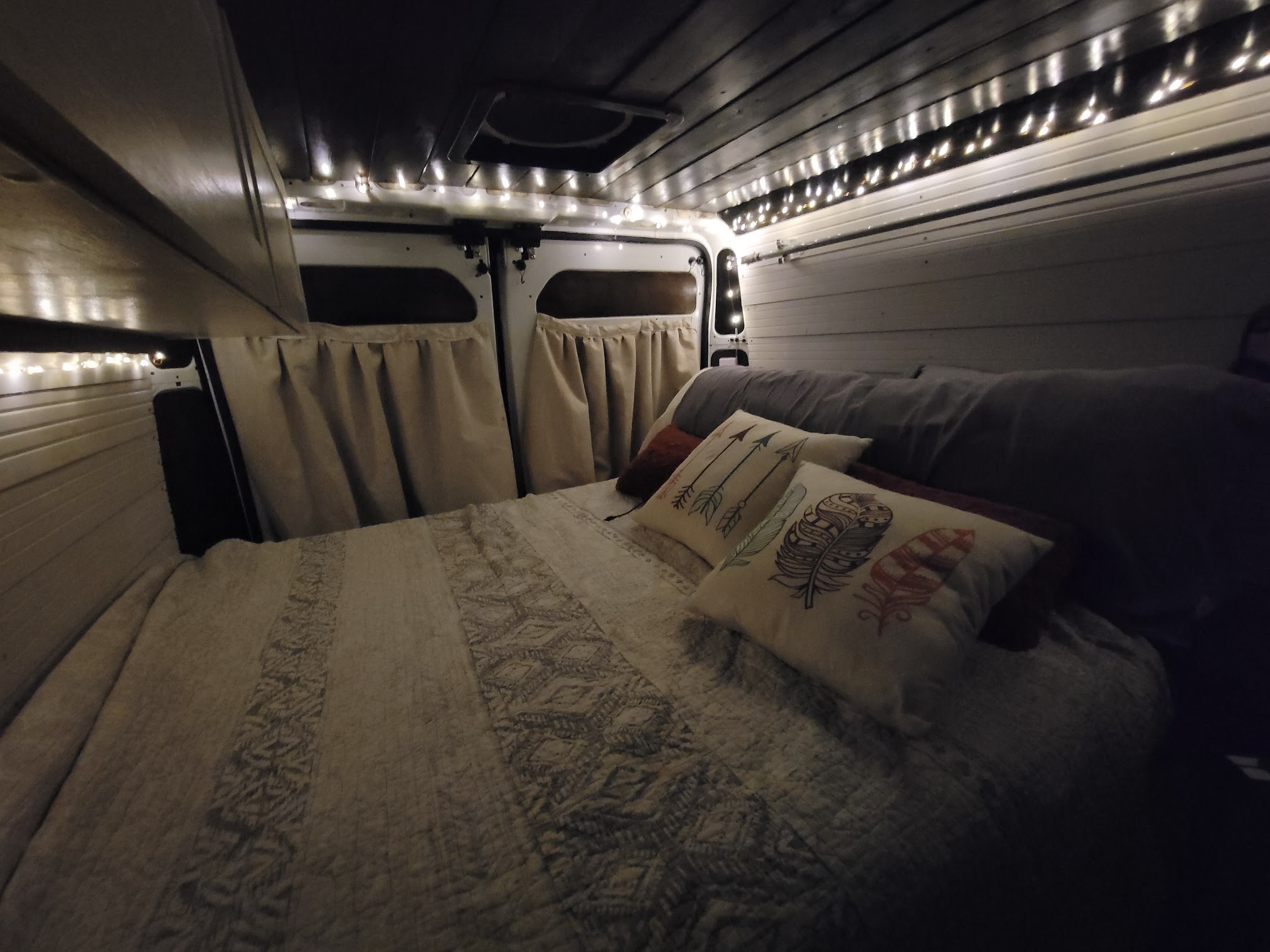 Experience a cozy night in this RV rental! Interior of a camper van bedroom with string lights, quilt, & pillows.. Dodge Promaster 2500 High Roof 2020