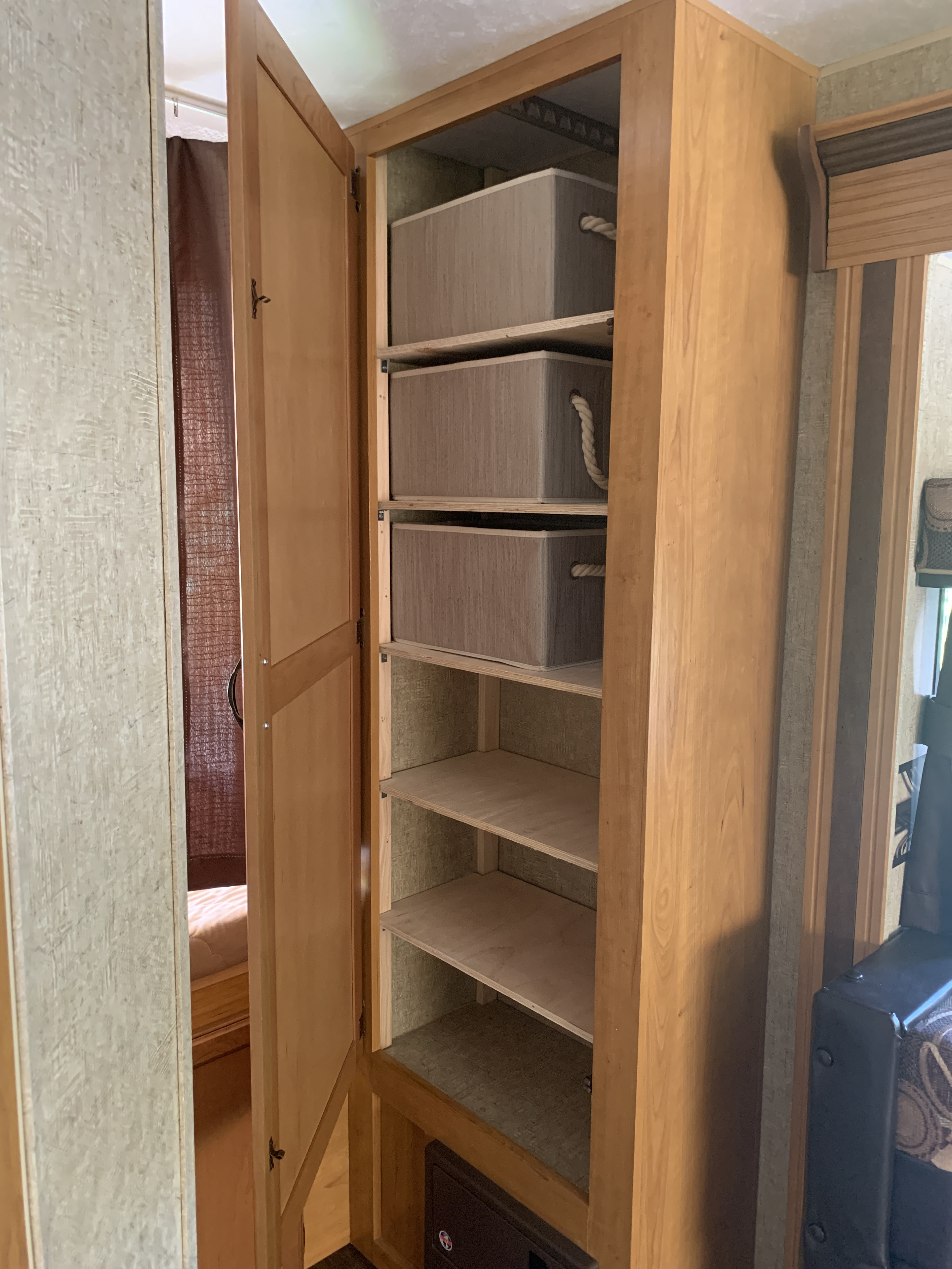RV rental interior showing an open wooden cabinet with several shelves. Three beige fabric bins are on the top shelves, with empty shelves below.. K-Z Manufacturing Spree 2015