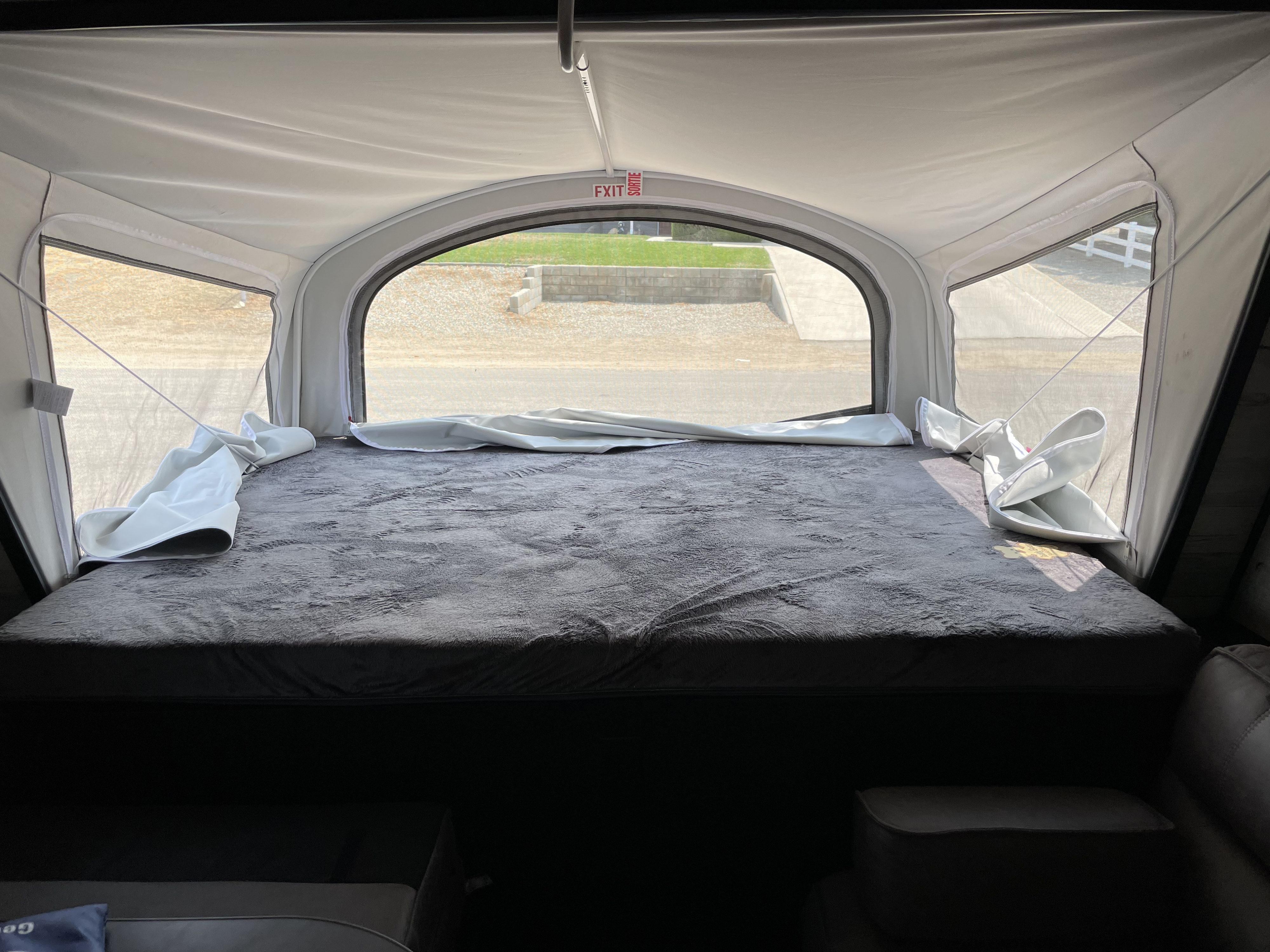Interior of an RV rental pop-up camper, featuring a plush bed, panoramic windows, and an exit sign.. Jayco Jay Feather 2021