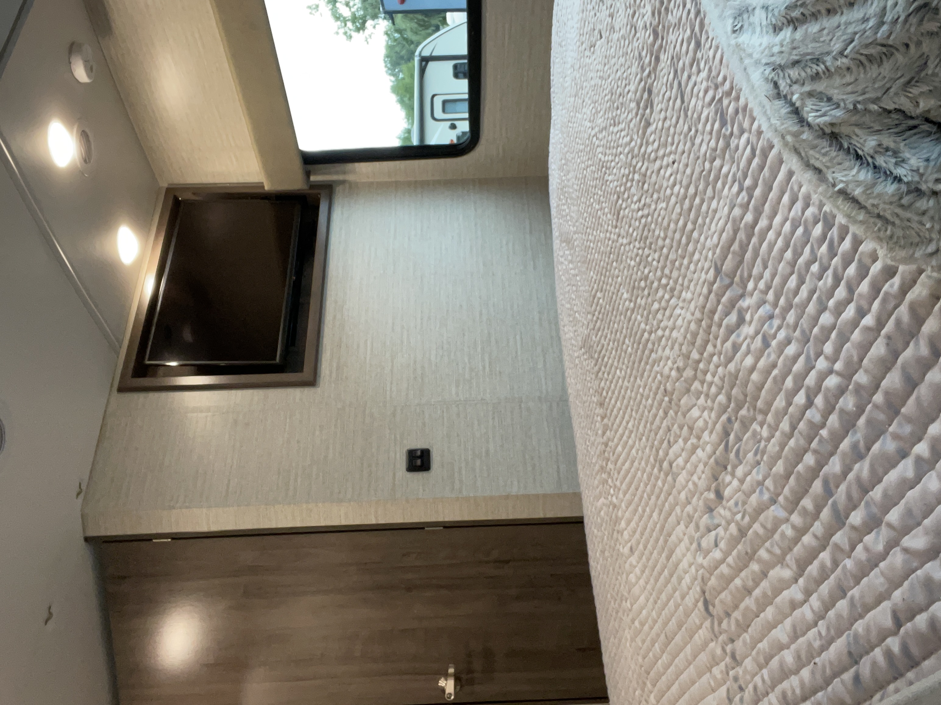 Cozy RV rental bedroom with a mounted TV, quilted bed, overhead lights, and a window showing another RV. Ideal for camping trips.. Winnebago Vista 2022