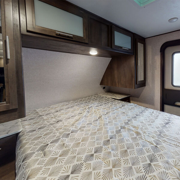 RV interior: A compact RV rental bedroom with a bed, patterned comforter, and ample overhead storage.. Dutchmen Other 2021