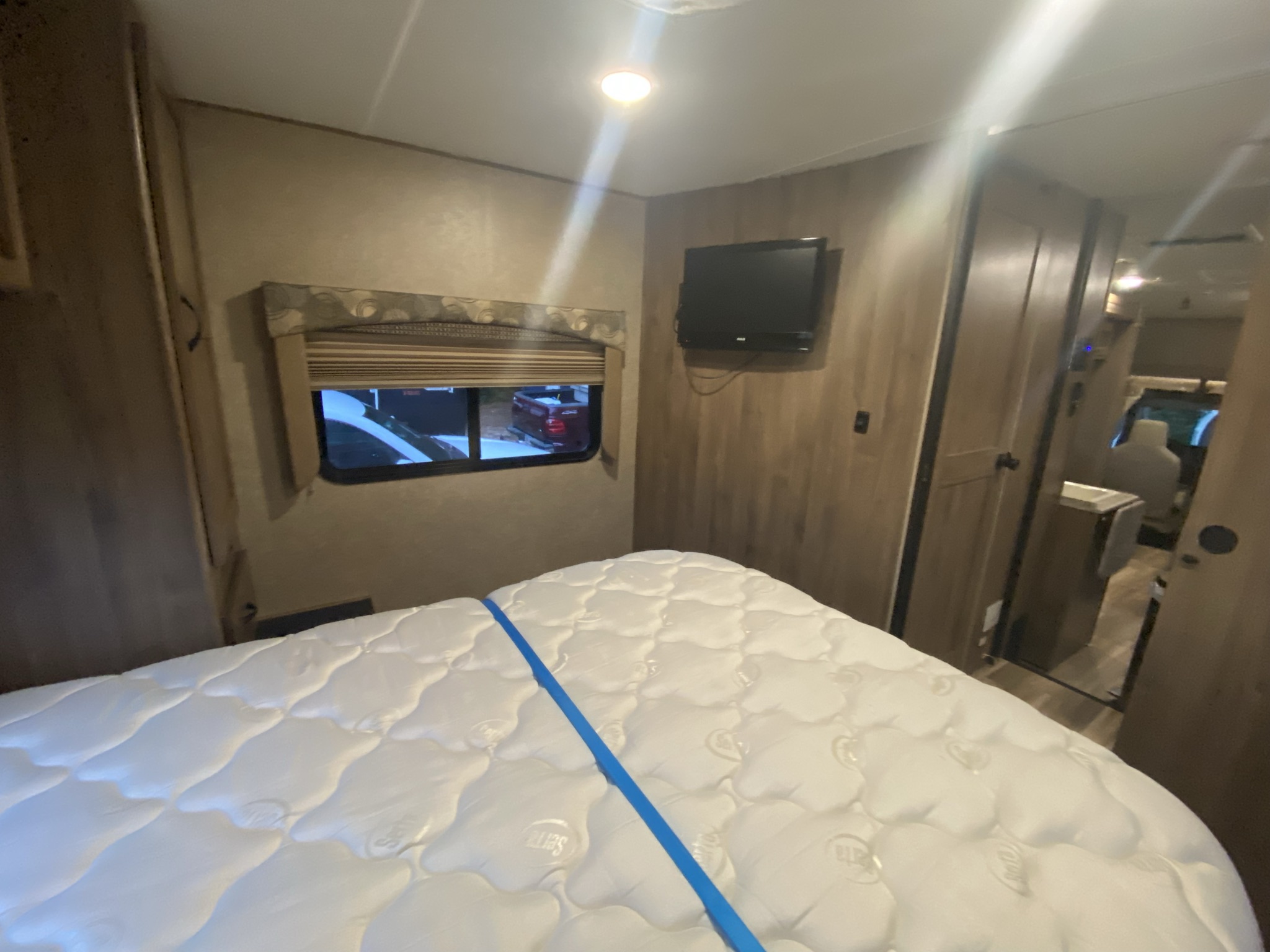 RV rental bedroom with a fresh Serta mattress, wall-mounted TV, and window views. Cozy interior space.. Coachmen Freelander 2016