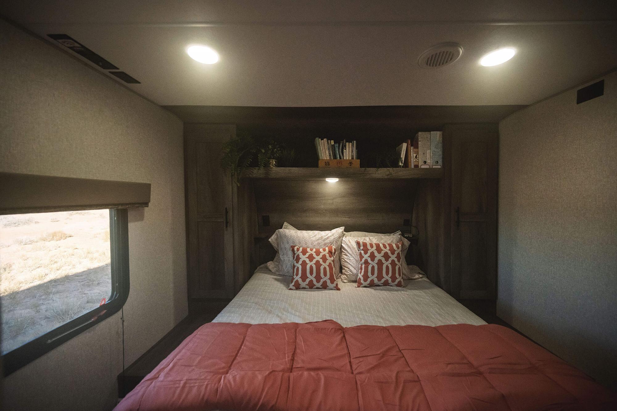 Inside this cozy RV rental bedroom: a bed with coral bedding, decorative pillows, overhead storage, and a desert view.. KZ Sportsmen 2021