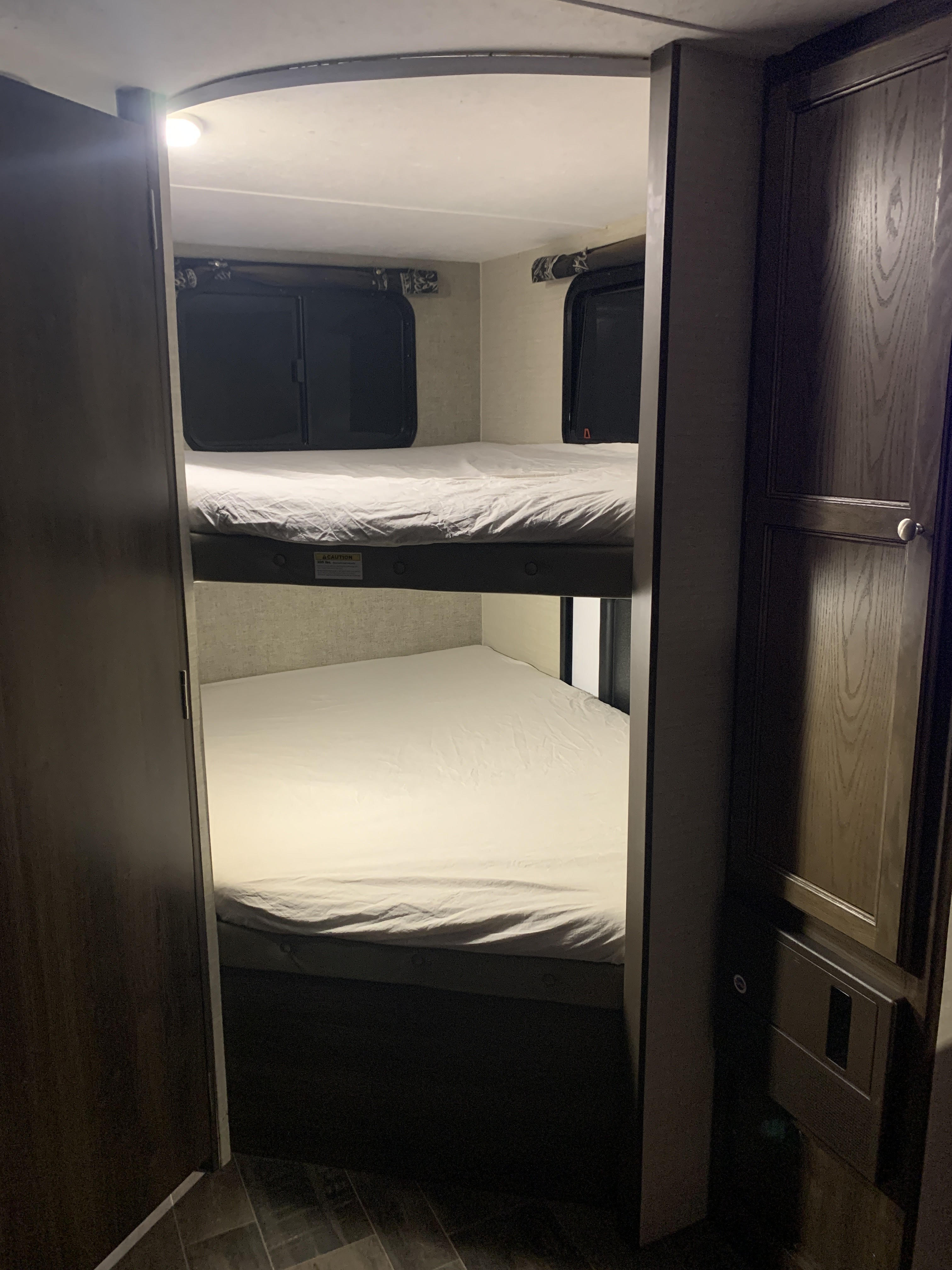 Cozy RV rental bunk beds, featuring two sleeping spaces with windows and white sheets. Perfect for family camping trips.. Keystone RV Bullet Ultra Lite 2017
