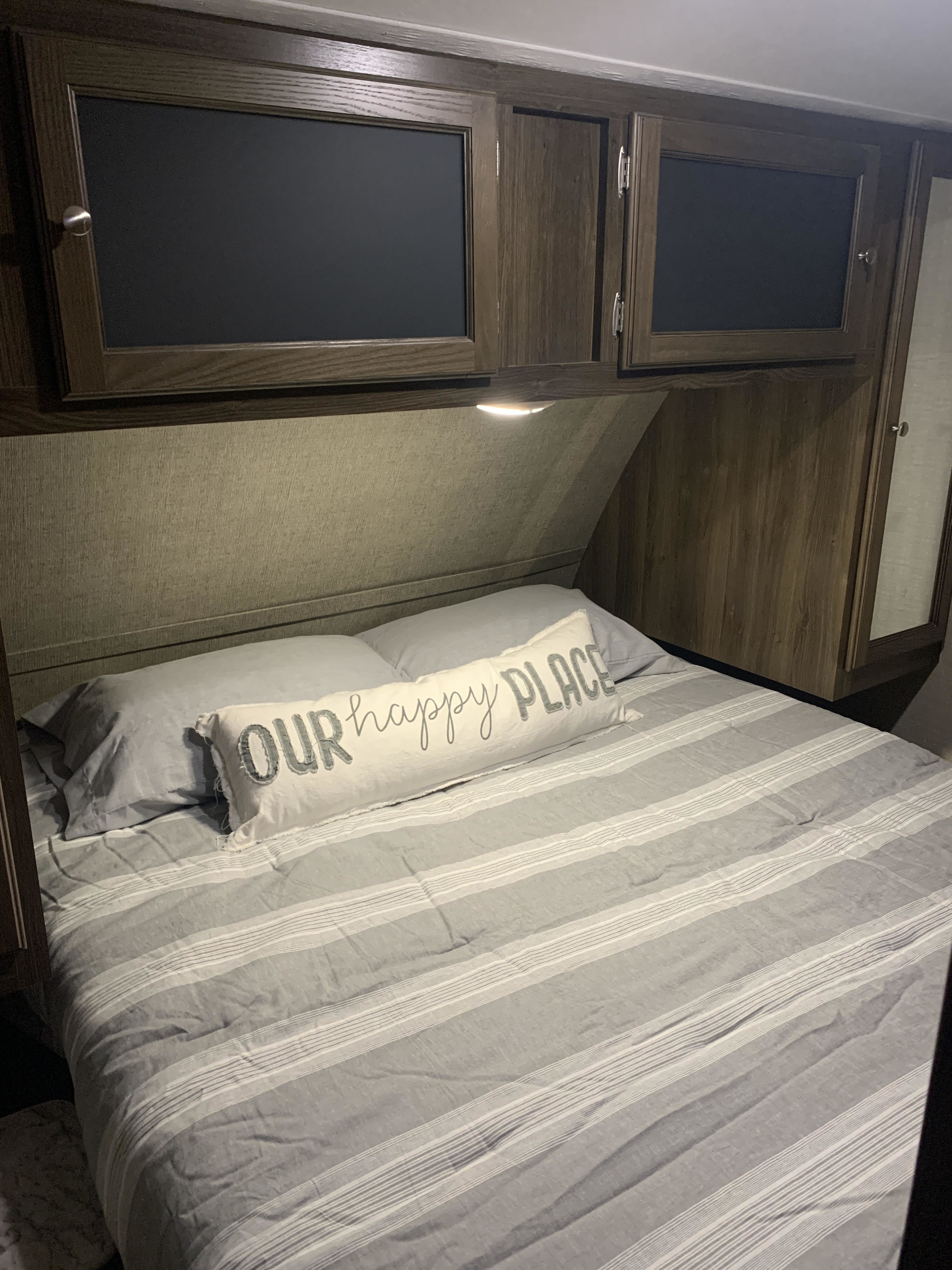 Cozy RV rental bedroom featuring a striped bedspread, "OUR happy PLACE" pillow, and ample overhead storage cabinets.. Keystone RV Bullet Ultra Lite 2017