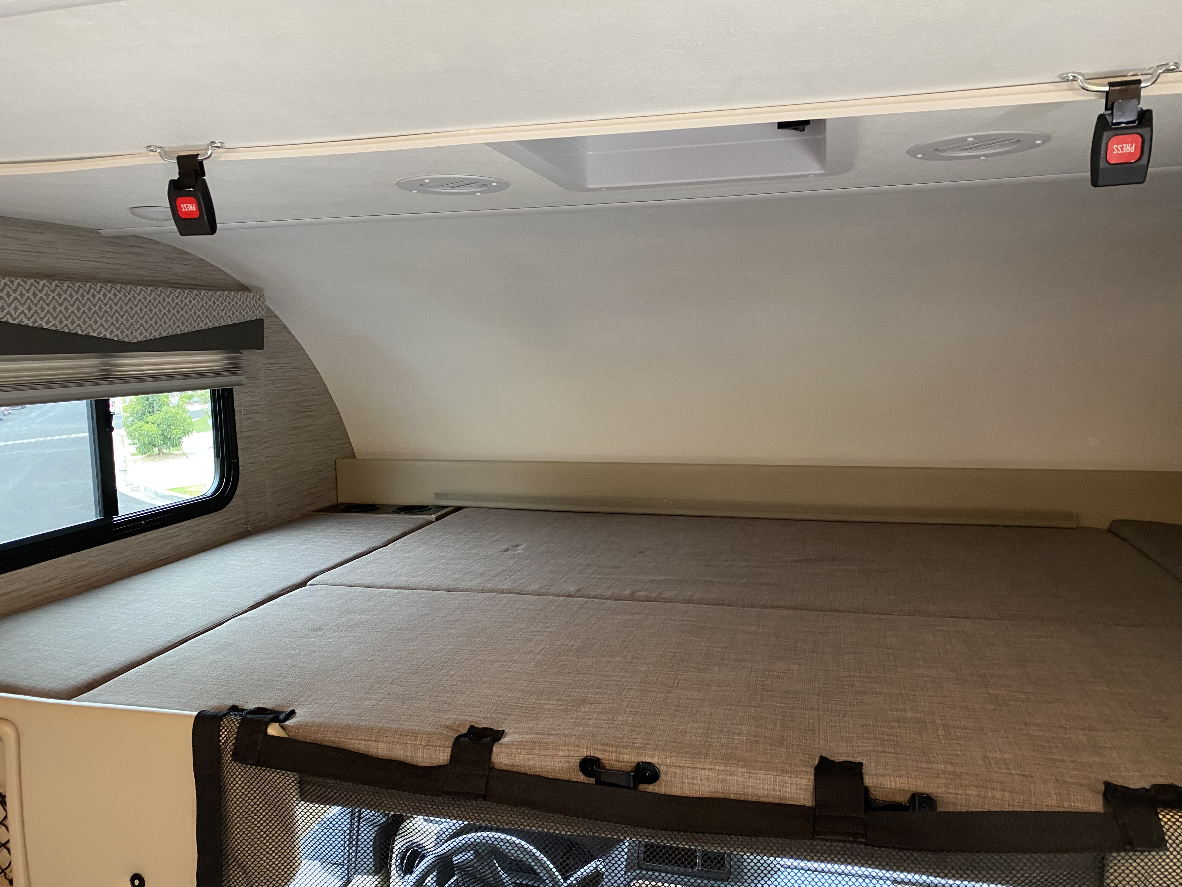 An RV rental motorhome's cab-over sleeping area with mattress, window, lights, and safety buckles.. Thor Four Winds 2022