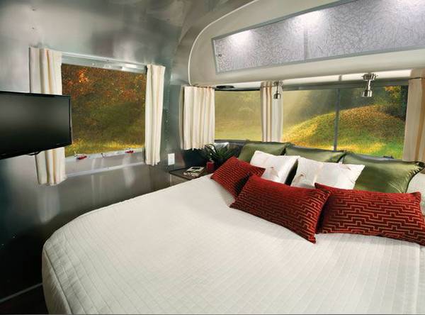 Modern RV rental bedroom. Sleek interior with large bed, TV, and big windows showing lush outdoor scenery.. Airstream International 2016