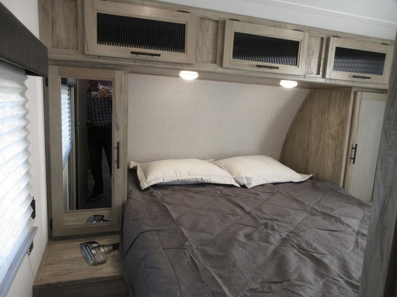 Cozy RV rental bedroom with a gray bed, overhead cabinets, and mirrored closet reflecting a person, ideal for travel.. Forest River 30DBH-L 2021