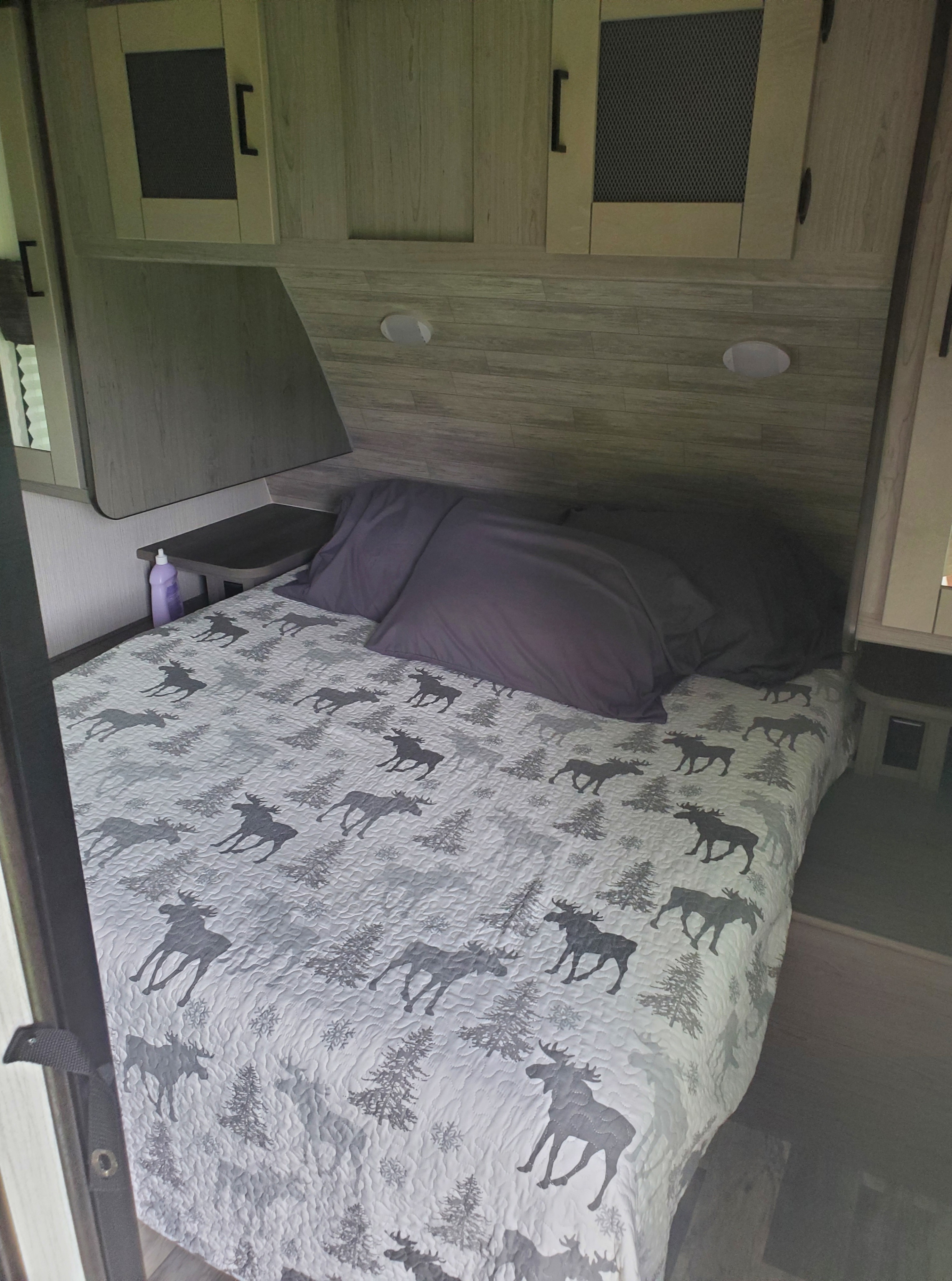 Cozy RV rental bedroom with a bed, gray moose quilt, and wood-paneled walls and cabinets.. Heartland RVs Mallard 2020