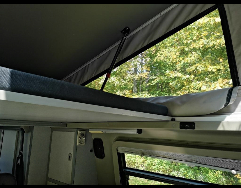 Inside your rv rental: a cozy pop-top bed overlooks lush forest. Enjoy elevated sleeping & nature views for your next adventure!. Winnebago Eurovan Camper Eurovan Camper 1997