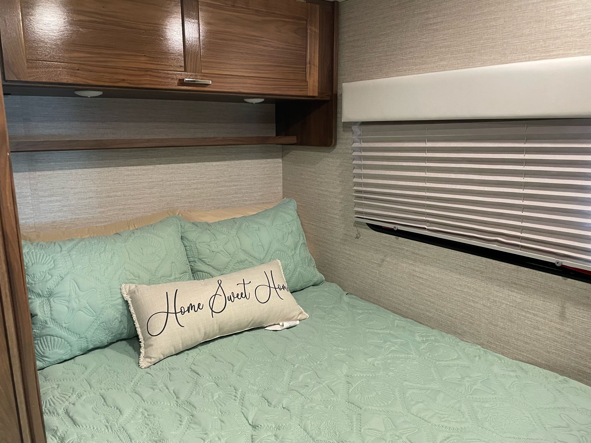 Cozy RV rental bedroom featuring mint green seashell bedding, "Home Sweet Home" pillow, and wooden cabinets above the bed.. Winnebago Outlook 2020