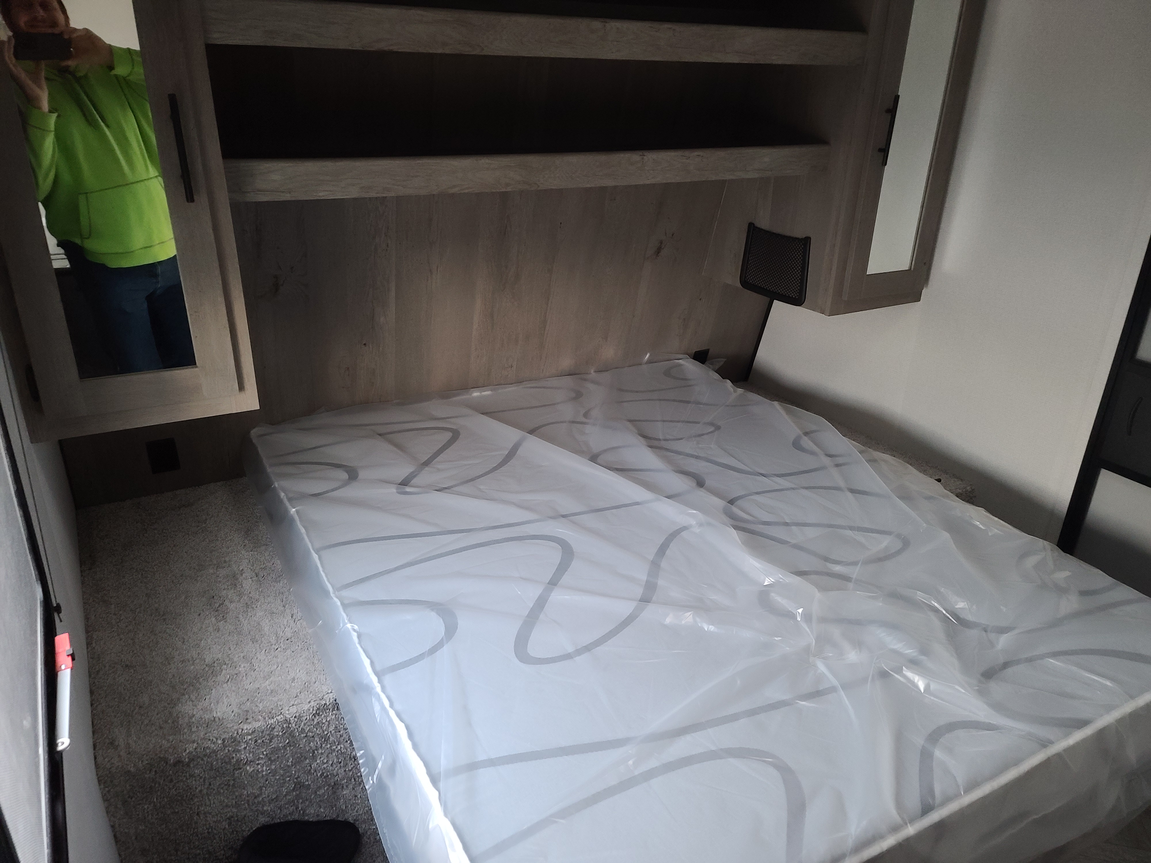 Experience comfort in this RV rental bedroom. It features a new, plastic-covered mattress, built-in shelving, and carpeted floors.. Keystone Springdale 2021