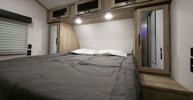 Inside a modern RV rental: a cozy bedroom with a comfortable bed, overhead storage, and window blinds.. Forest River Cherokee Alpha Wolf 2022