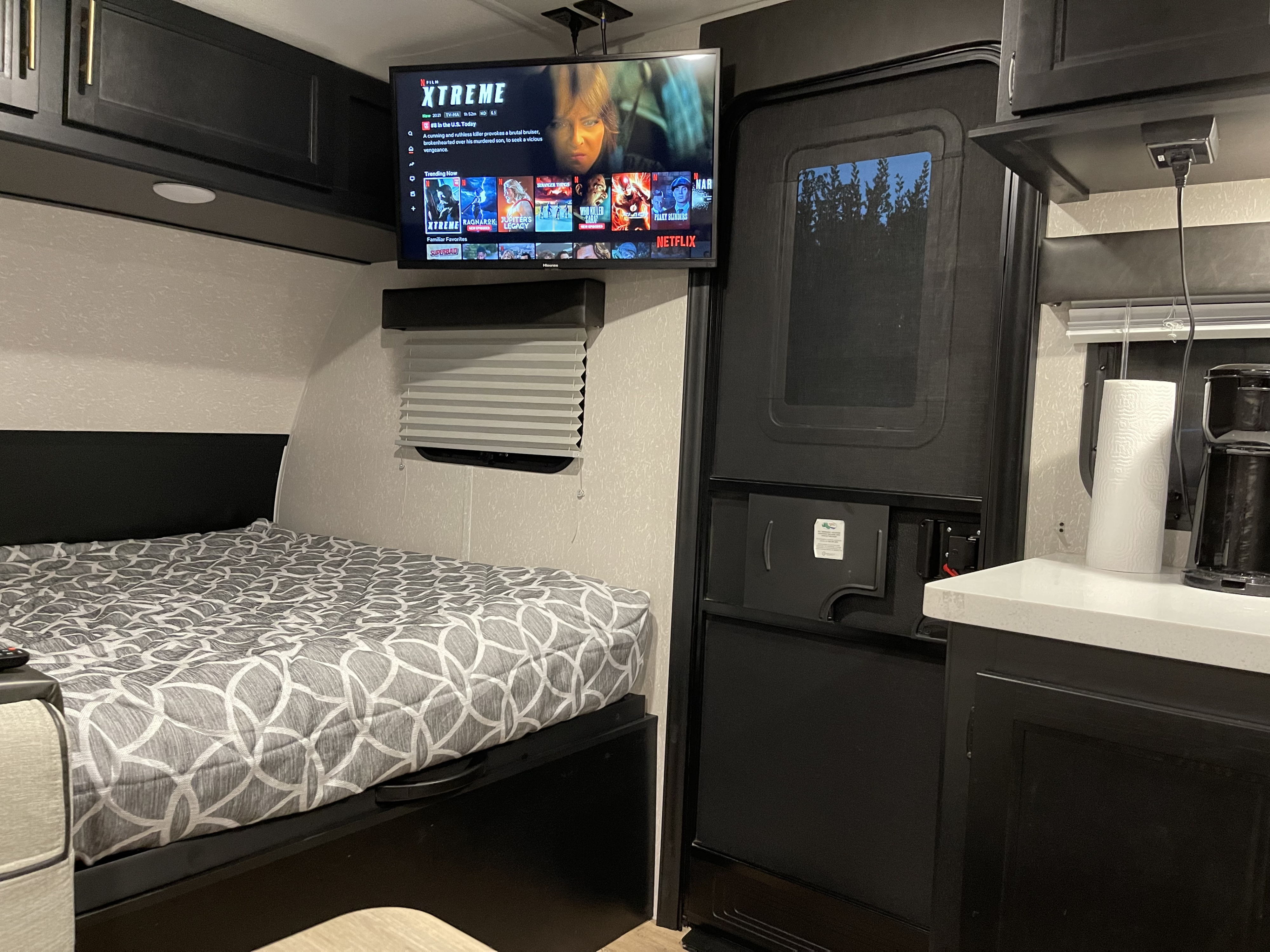 This RV rental interior features a cozy bedroom area with a TV for Netflix, and a functional kitchen counter.. Forest River Cherokee Wolf Pup Black Label 2021