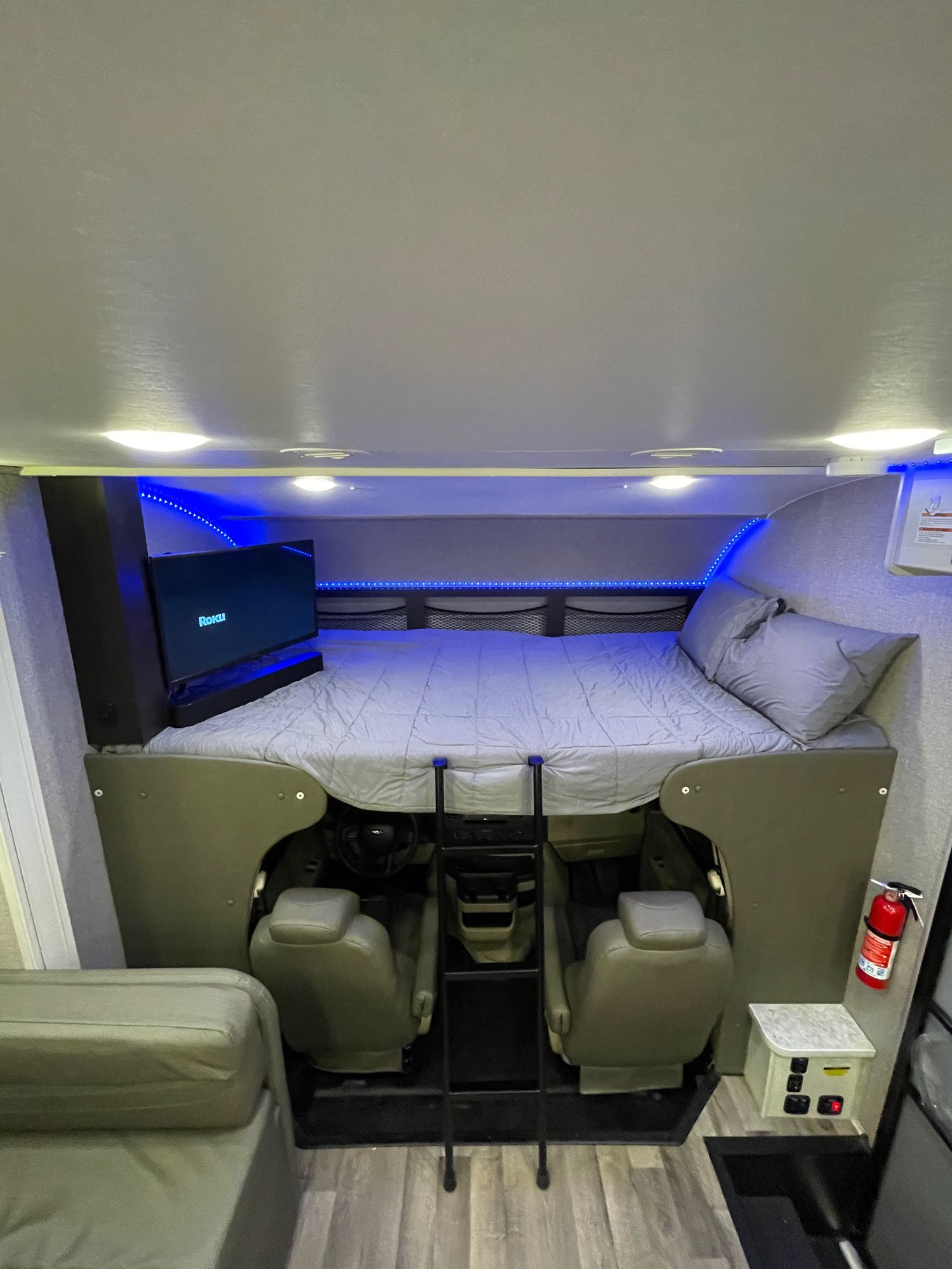 Cozy RV rental cab-over bunk featuring a bed, TV, and driver's cockpit below, illuminated by blue LED lights.. Jayco Redhawk 2021