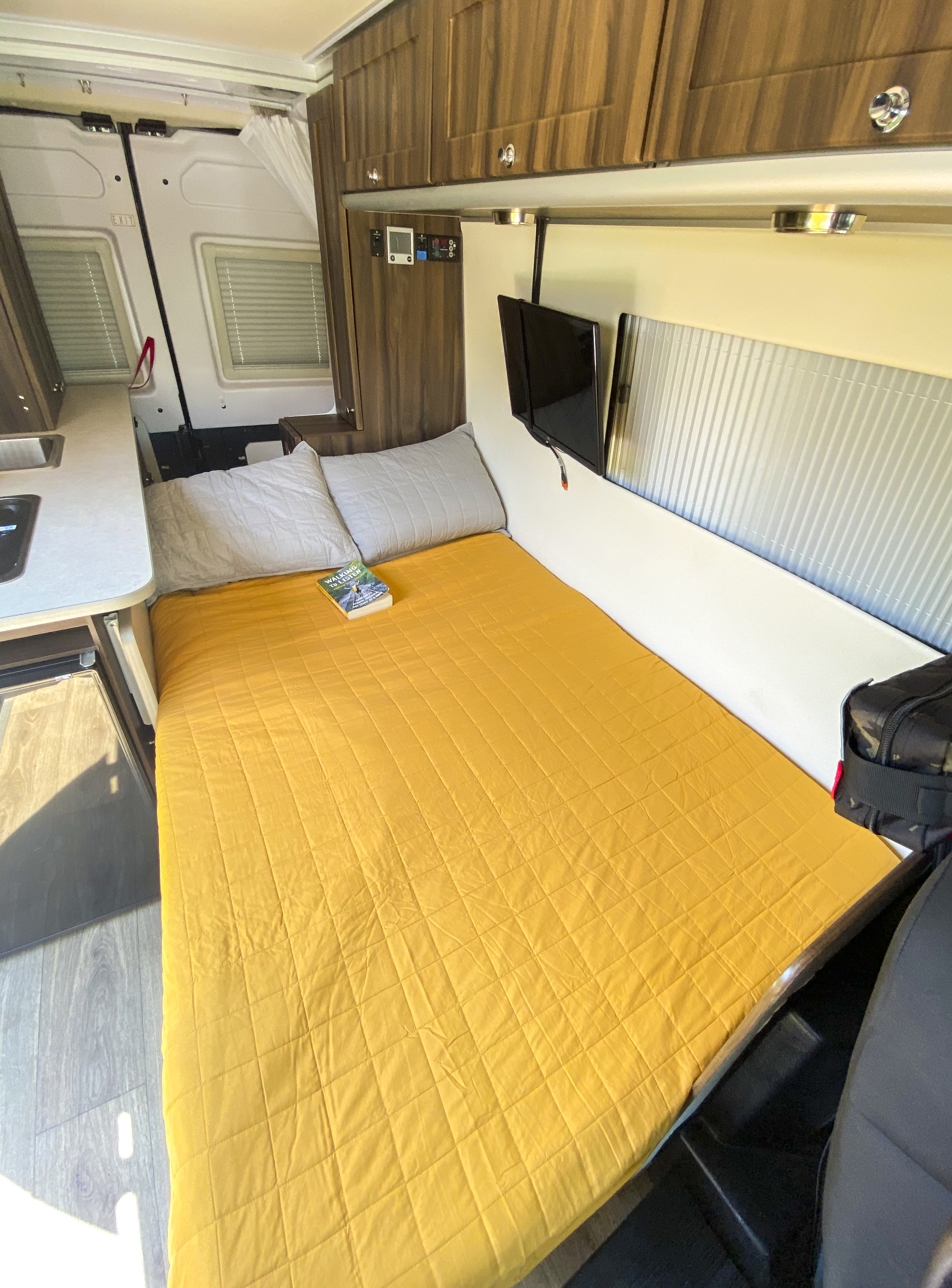 Spacious rv rental camper interior featuring a comfy bed, kitchenette, and wall-mounted TV for travel.. Hymer Axion Sprinter Van 2019