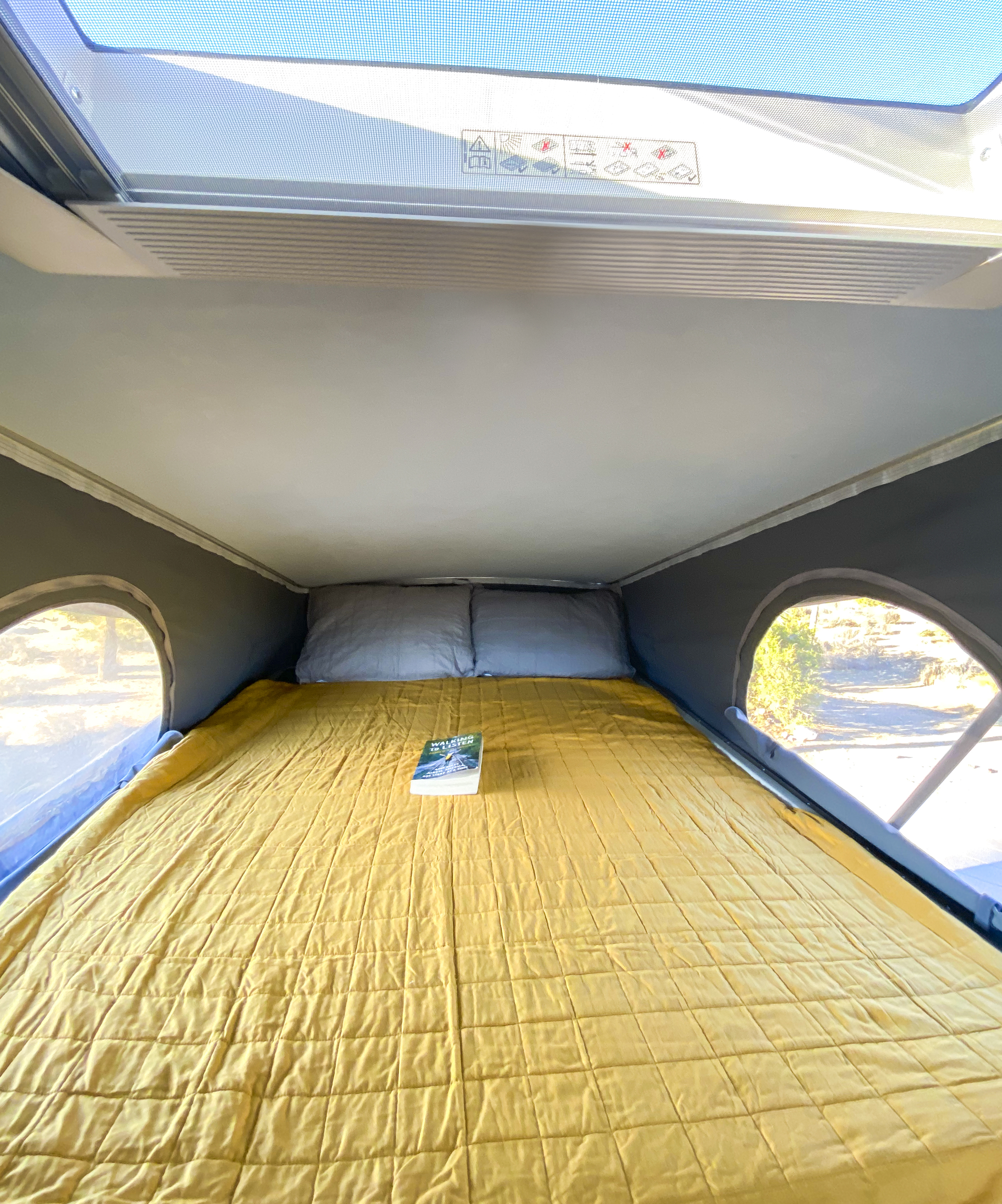 Bright yellow bed inside a pop-top RV rental, complete with pillows and a book. Ideal for travel and camping.. Hymer Axion Other 2019