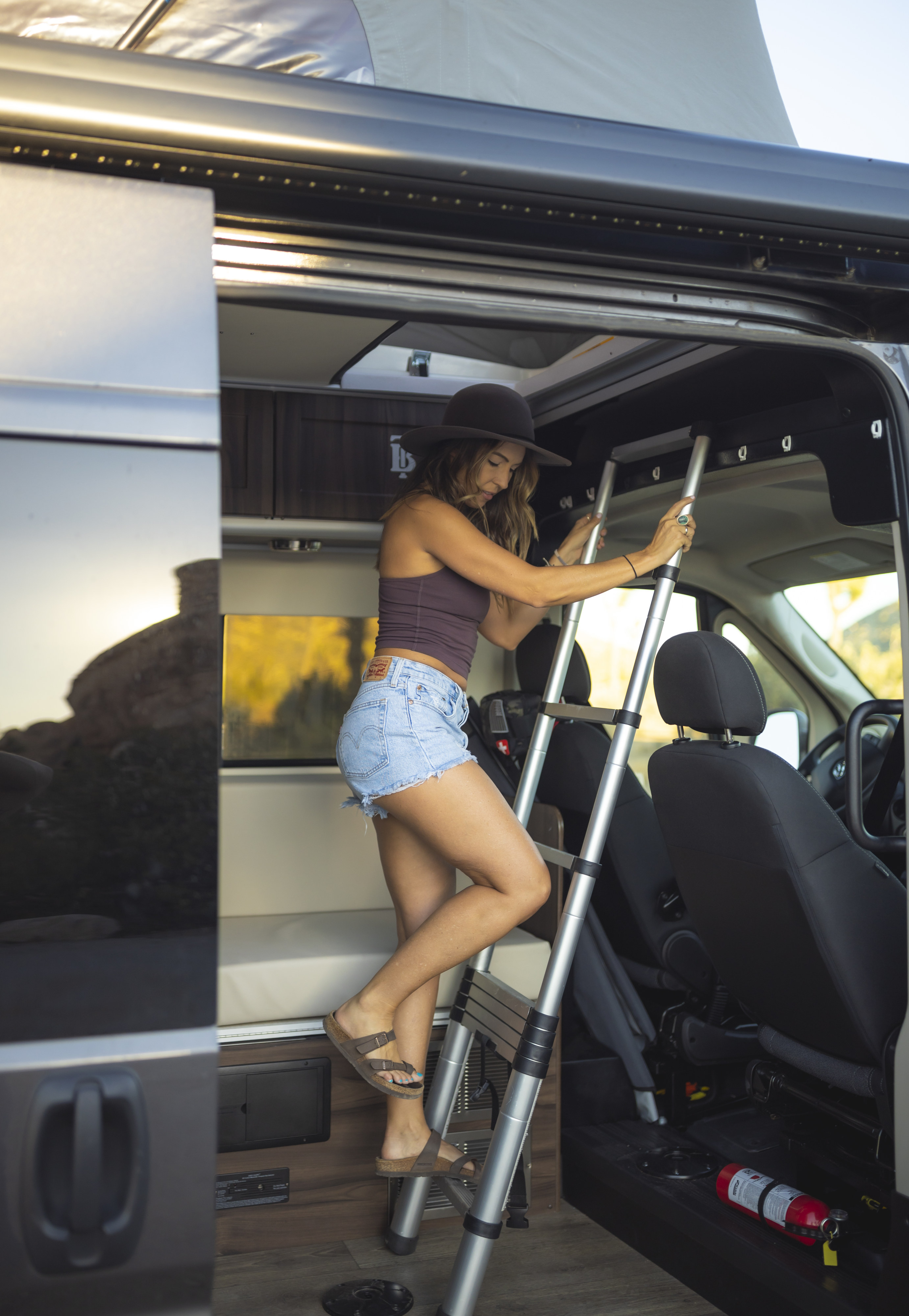 Woman climbing ladder in RV rental to reach the pop-top bed of this modern camper van.. Hymer Axion Other 2019
