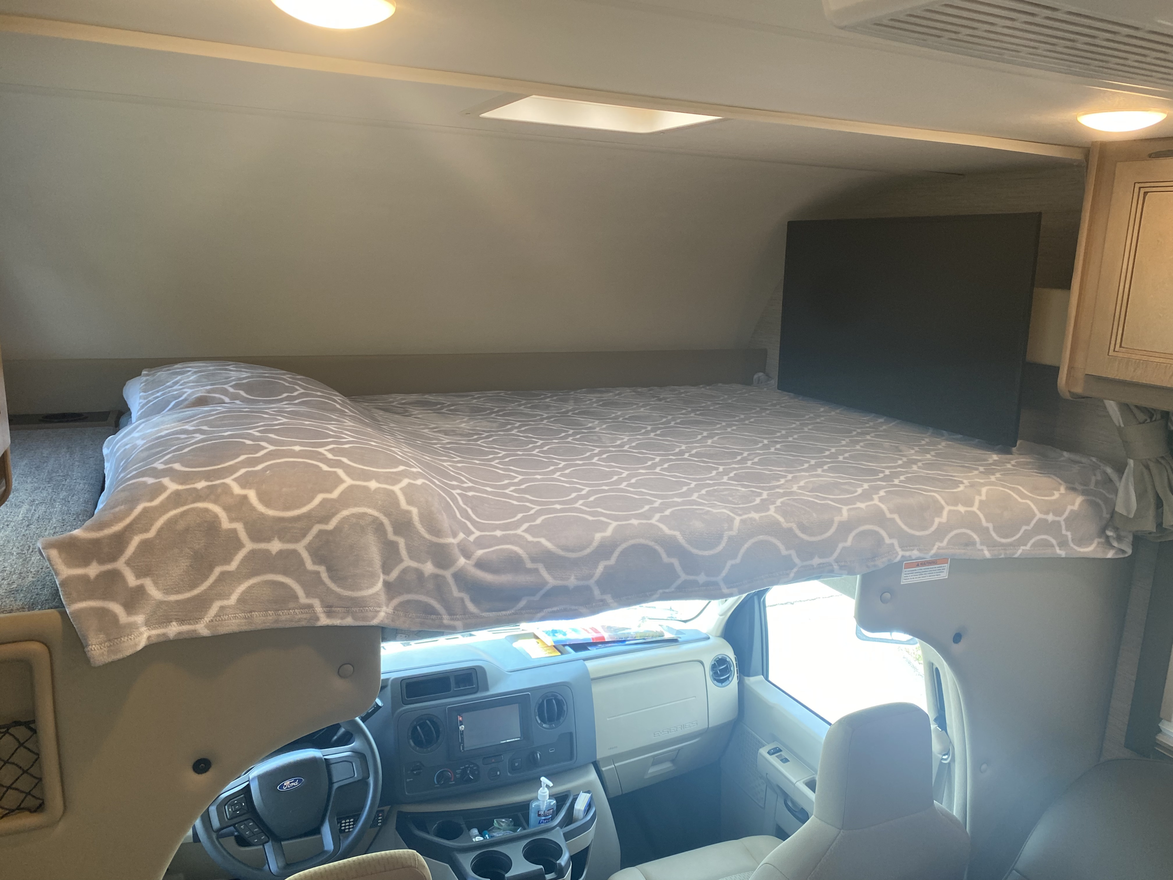 Cozy cab-over bunk and driver's cabin inside an RV rental, featuring a skylight and TV.. Thor Coleman 2022