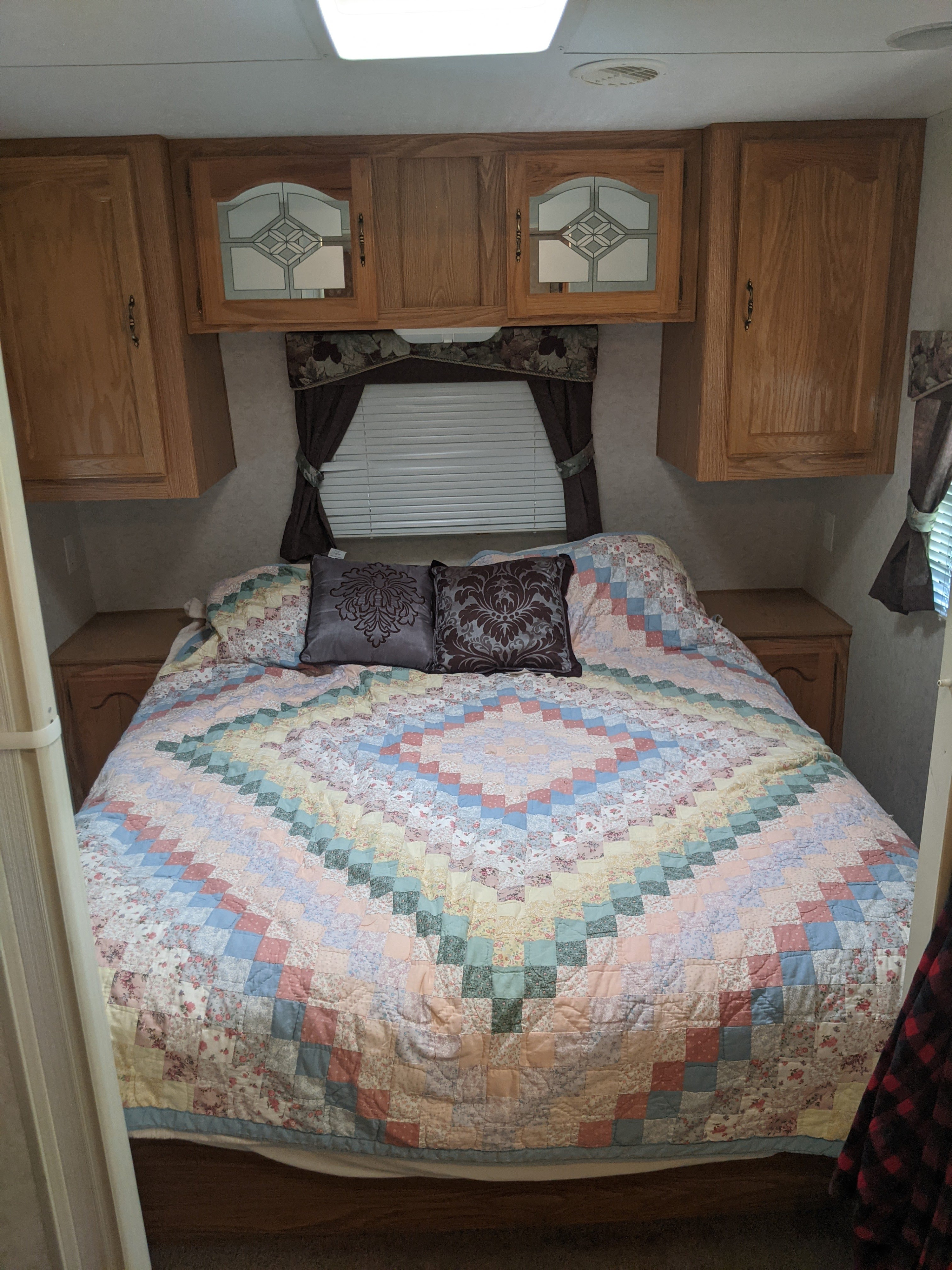 Cozy RV rental bedroom with a colorful quilted bed, patterned pillows, and practical wood overhead cabinets.. K-Z Manufacturing Sportsmen 2003