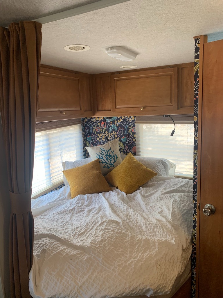 Comfortable RV rental bedroom interior with a neatly made bed, bright pillows, and overhead wood cabinets.. Winnebago Chalet 2010