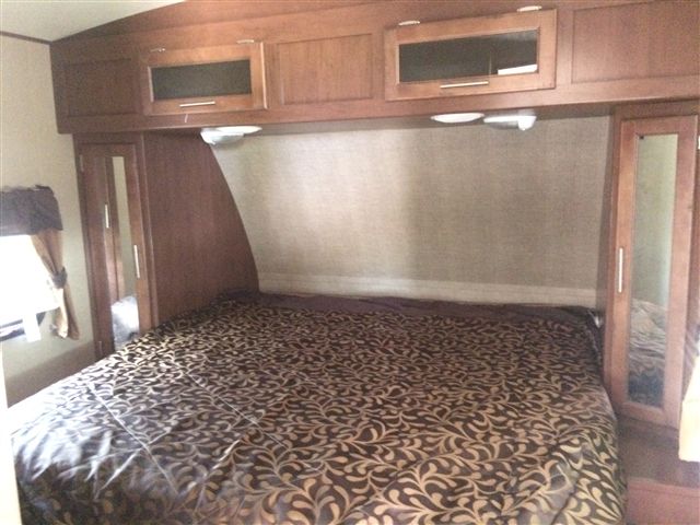 RV rental bedroom showing a comfortable bed with patterned bedding, overhead cabinets, and mirrored side wardrobes.. Aerolite Aerolite Trailer 2014